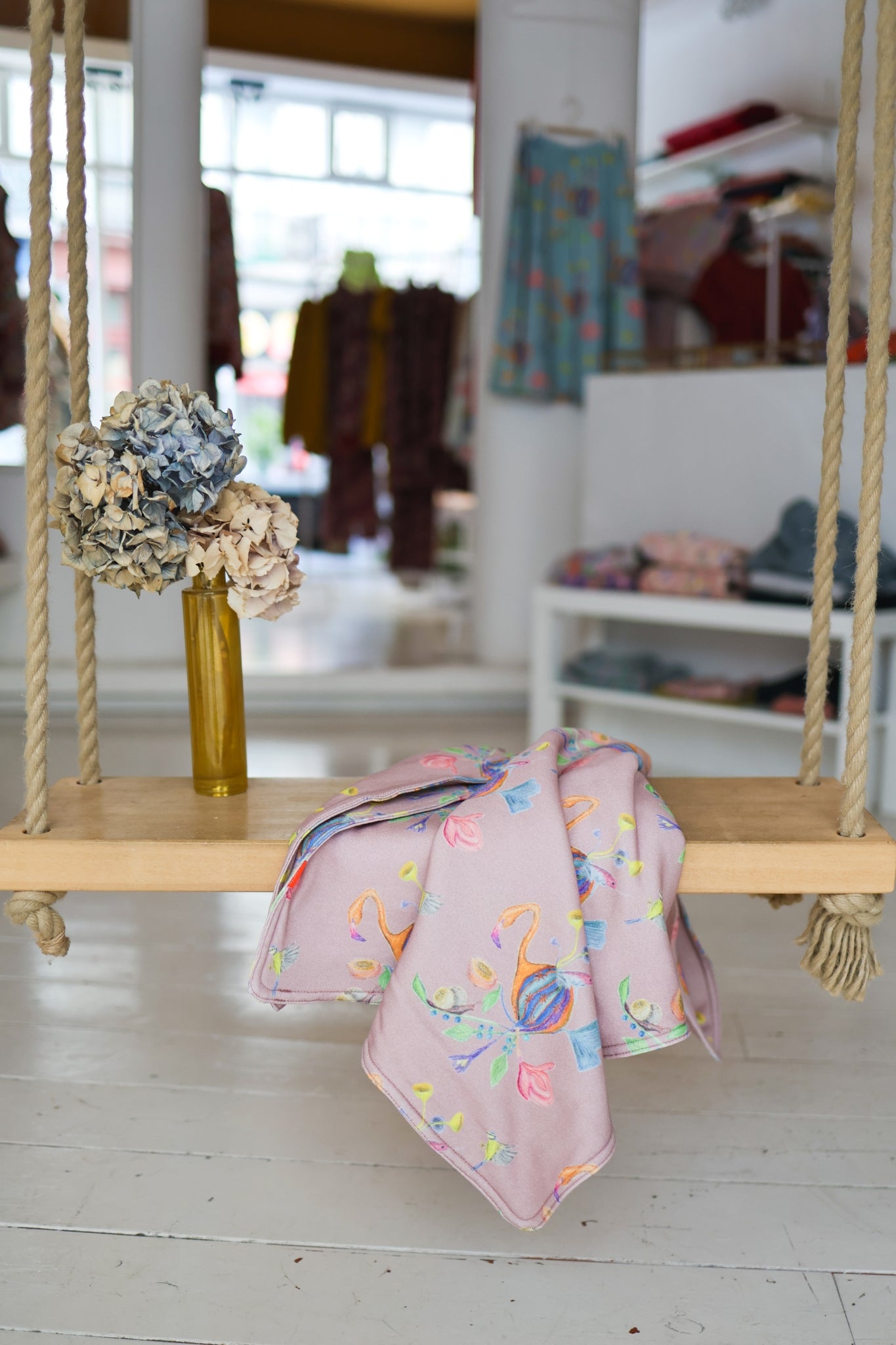 Pink babies blanket with colorful paterns on a wooden swing in a store setting.
