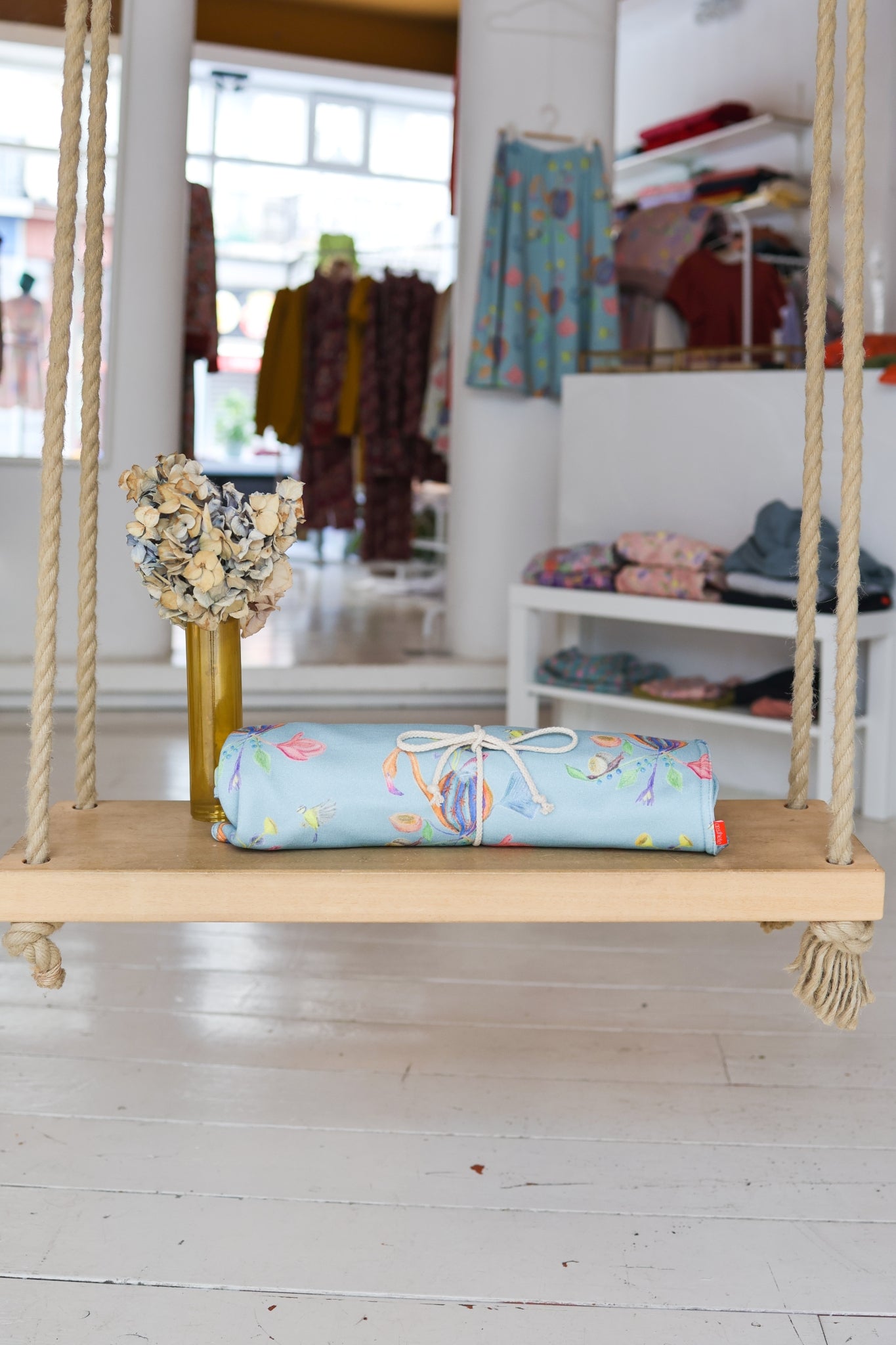 Wooden swing with a colorful babies blanket roll on a light wooden floor.