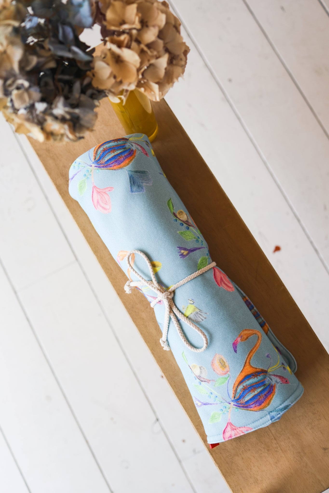Roll of babies blanket with flamingo pattern on a wooden surface.