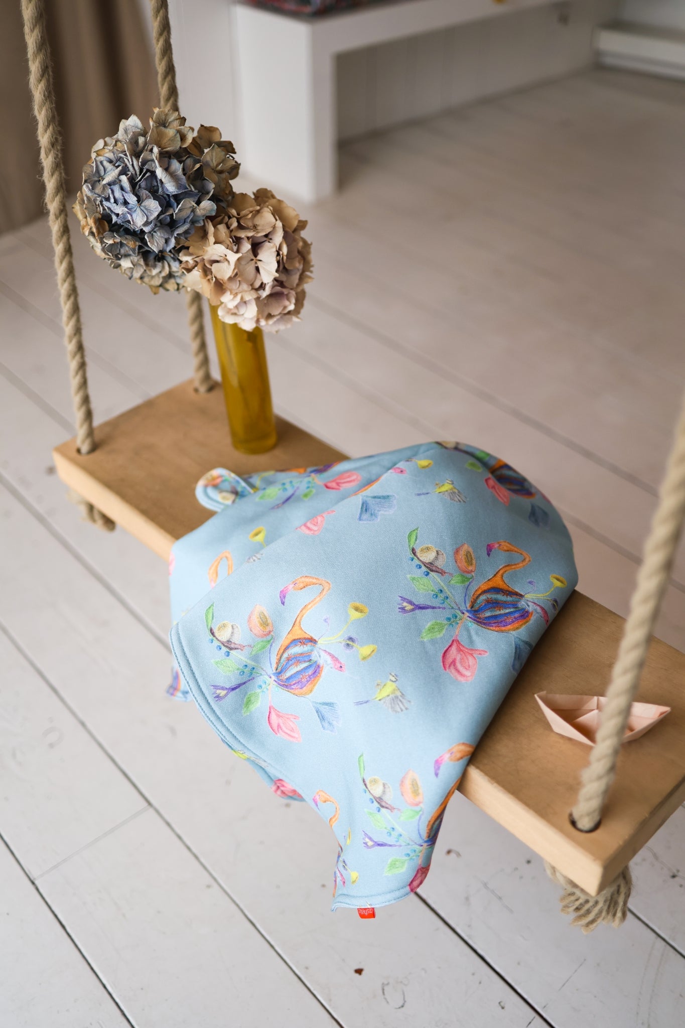 Colorful babies blanket on a wooden swing with decorative items in a store setting.