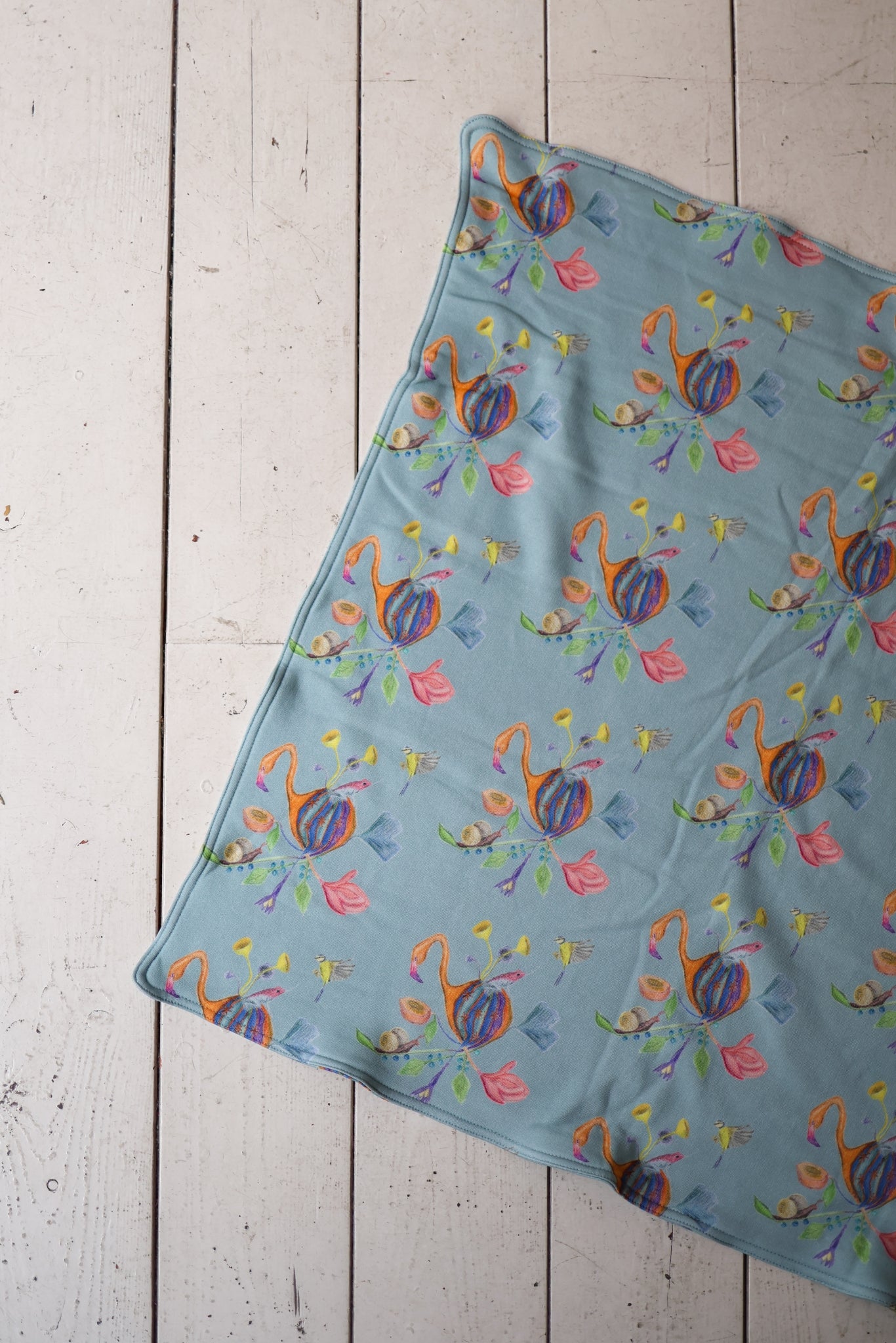 Colorful flamingo patterned babies blanket on a wooden surface.