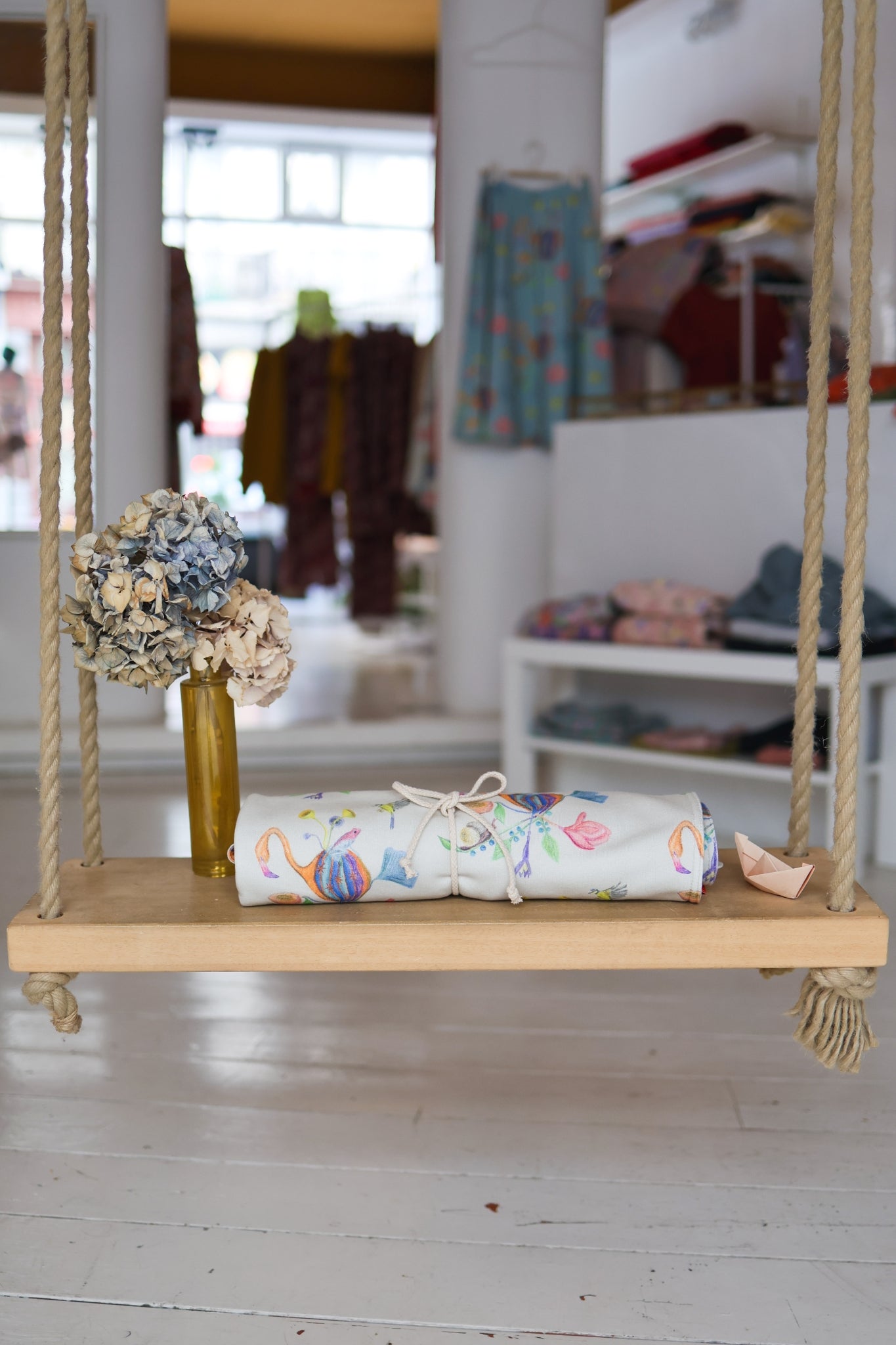 Wooden swing with rolled-up babies blanket and flowers in a store setting.