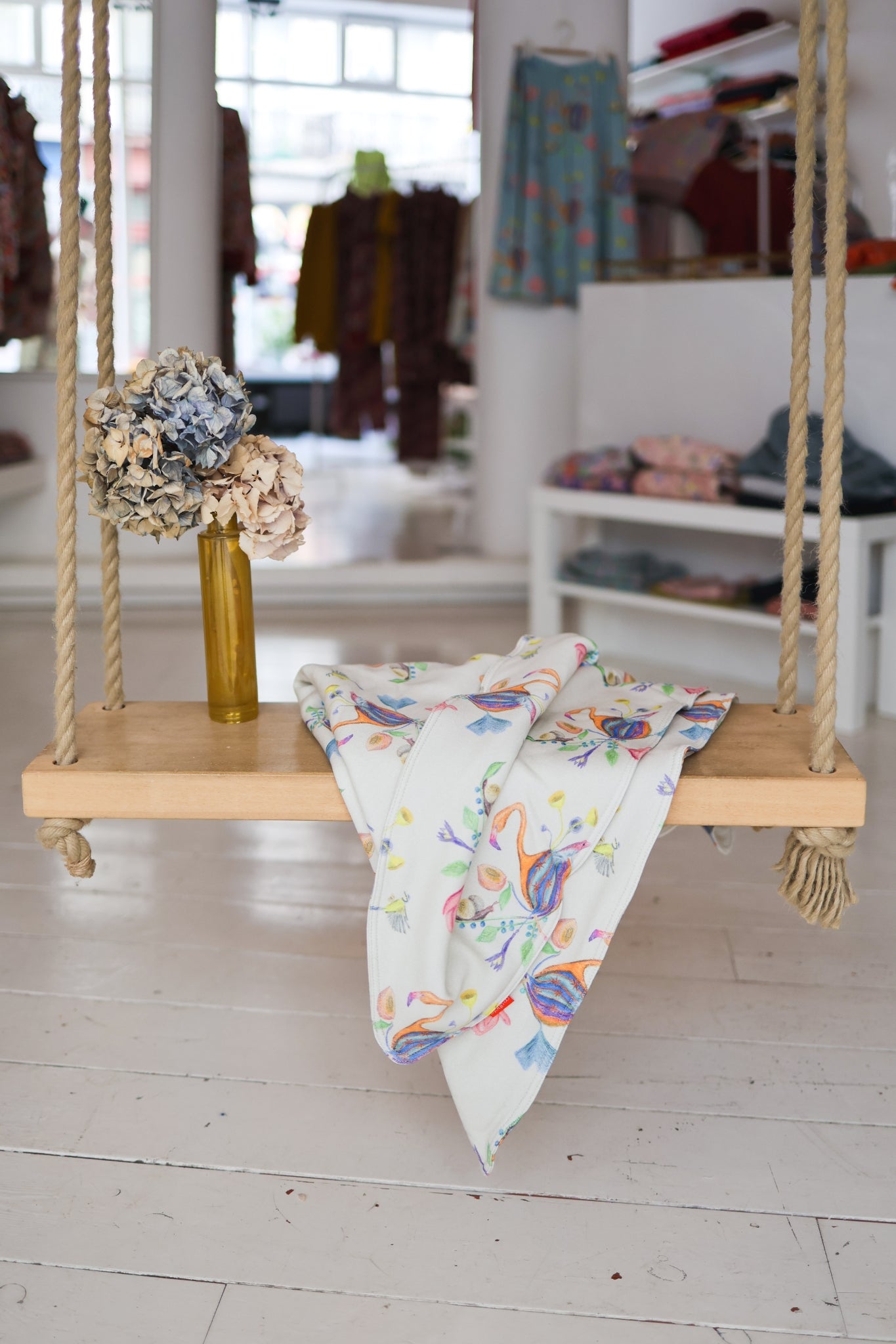 Wooden swing with a colorful babies blanket and flowers in a store setting.