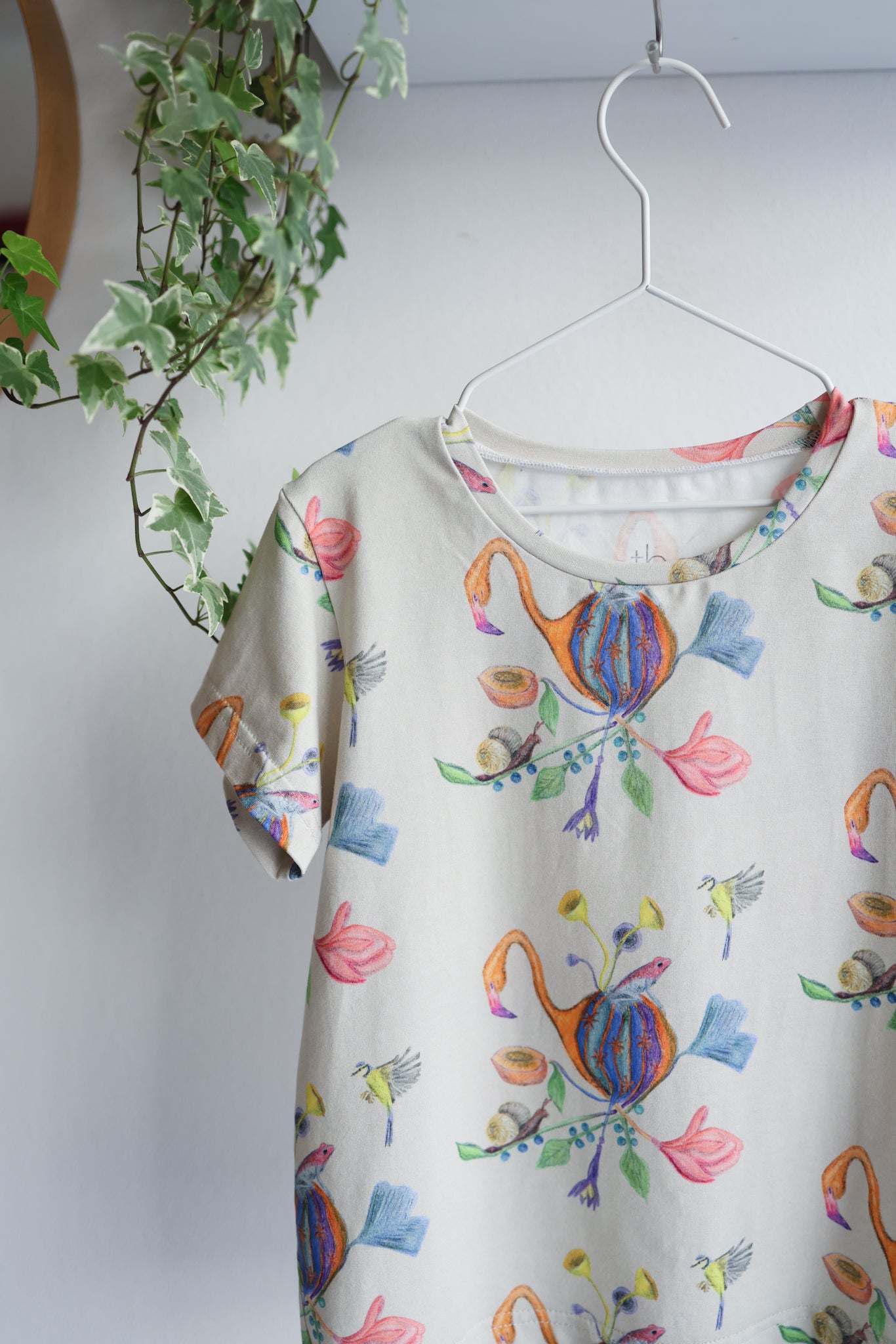 Colorful t-shirt with abstract designs on a hanger against a white wall.