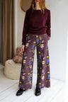 Woman wearing a sweater and patterned pants in a room with a white wall and wooden floor.