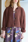 Woman wearing a brown jacket over a patterned dress in a room with a blurred background.
