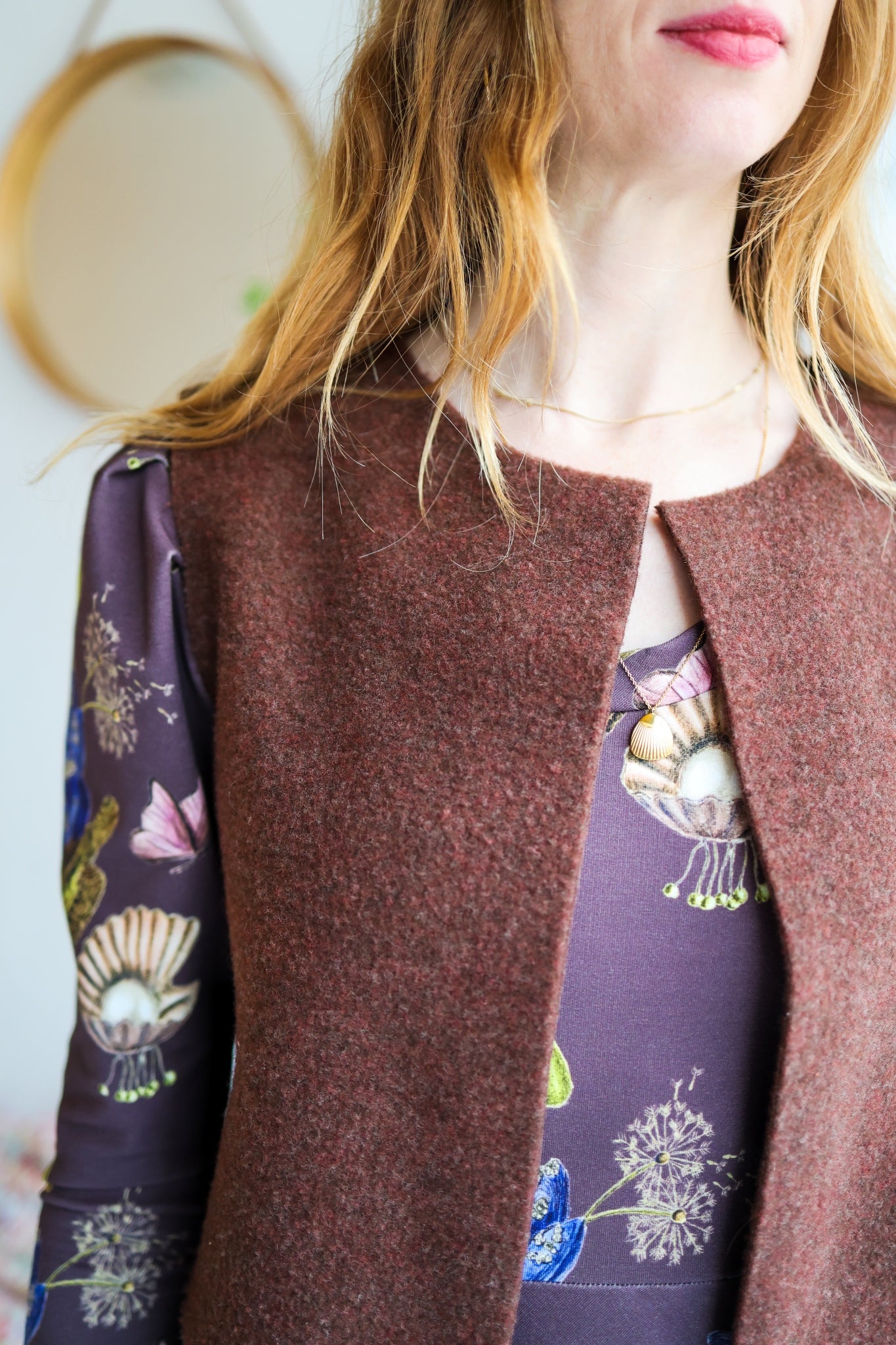 Close-up of a woman wearing a brown vest over a patterned dress with a blurred background.