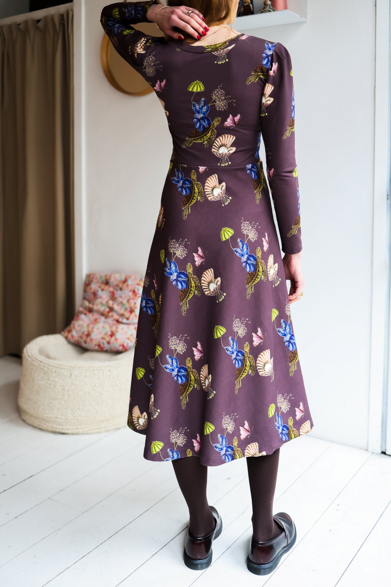 Woman wearing a patterned dress with long sleeves in a room with a white wall.