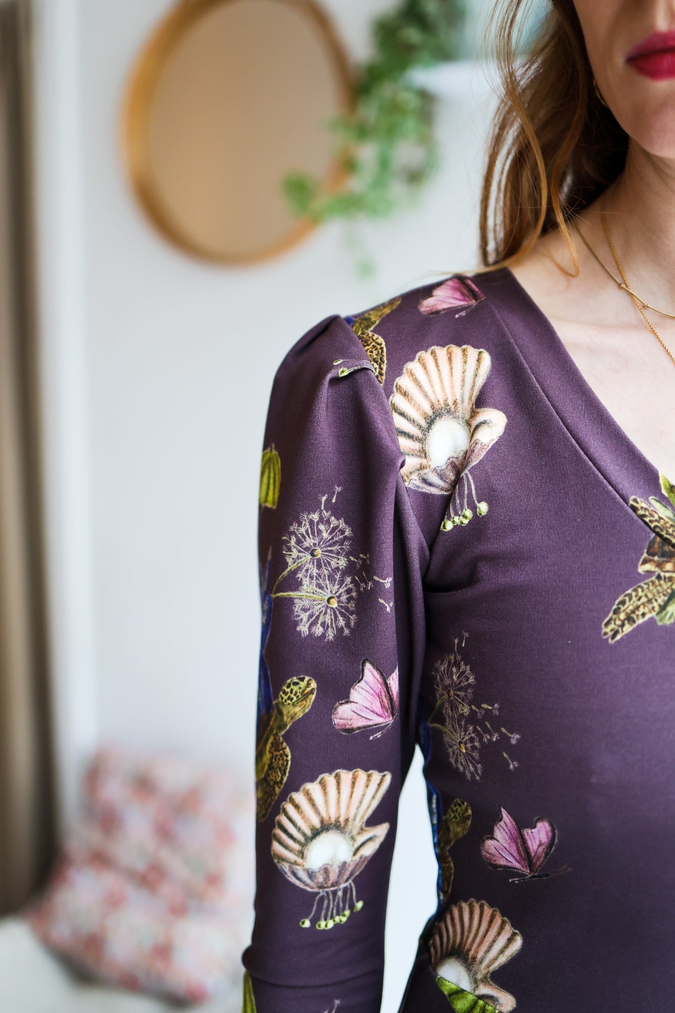 Woman wearing a patterned dress with long sleeves in a room with a blurred background.
