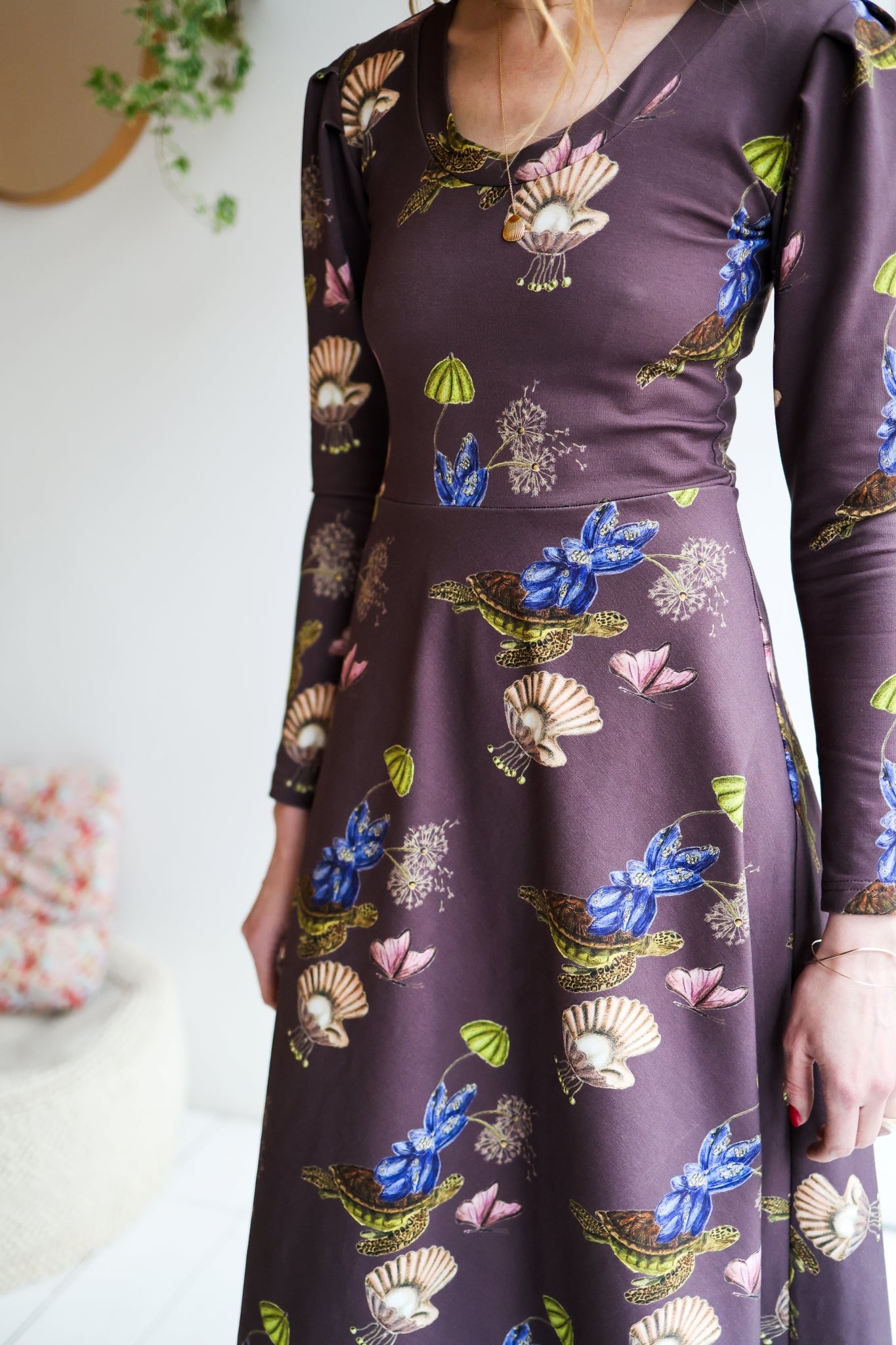 Woman wearing a patterned dress with long sleeves in a room with a white wall.