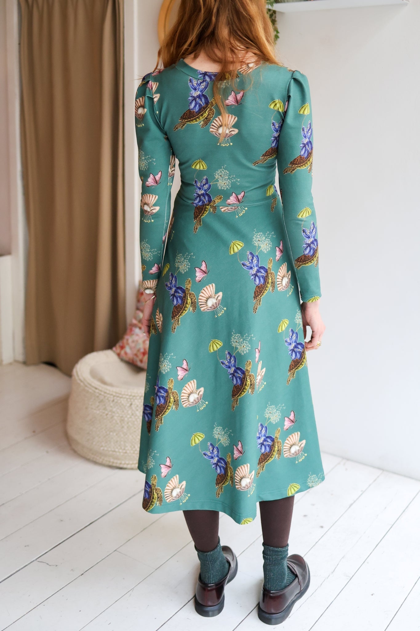 Woman wearing a teal dress with floral pattern in a room.