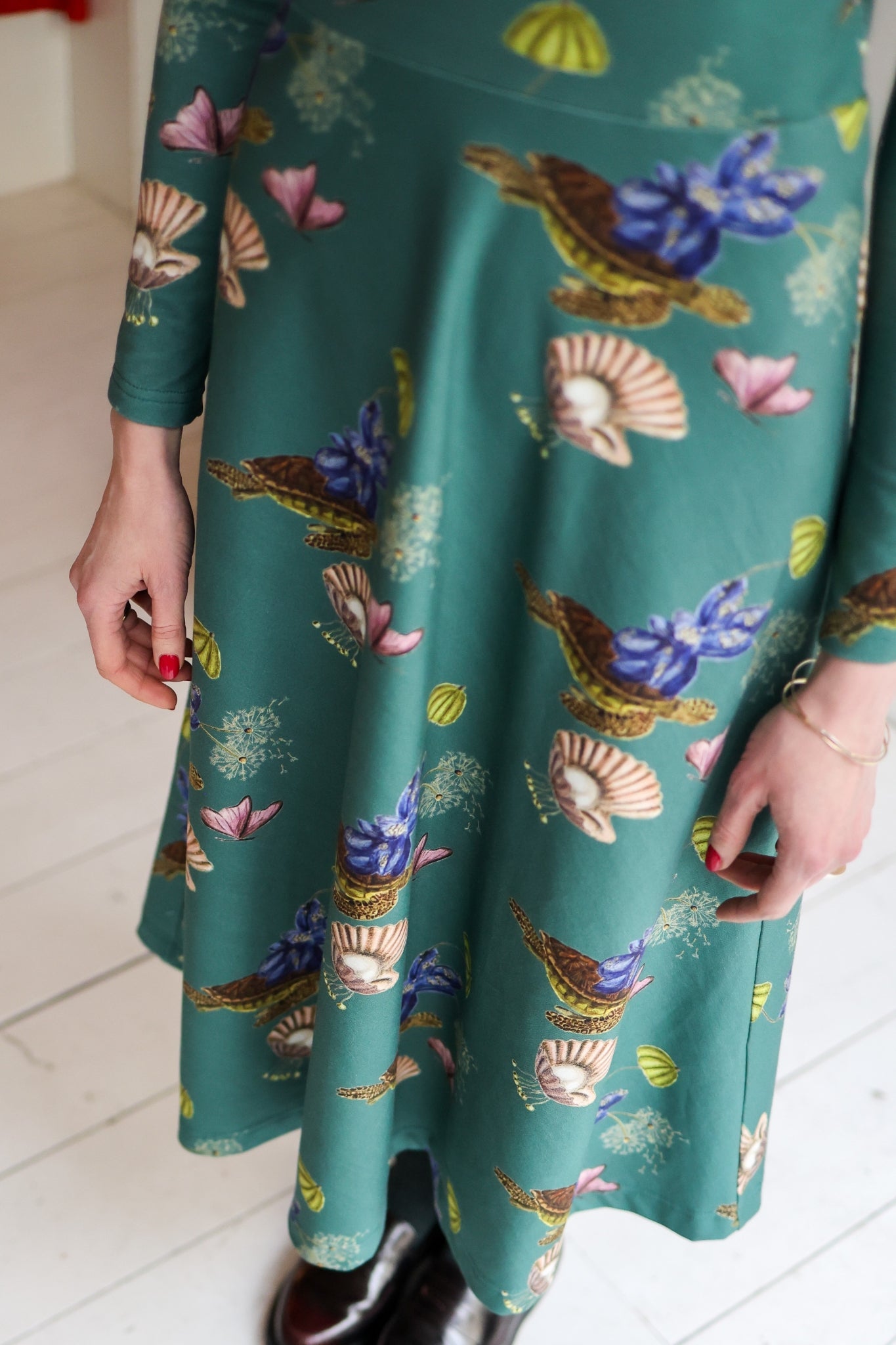 Green dress with colorful shell pattern worn by a woman on a white floor.
