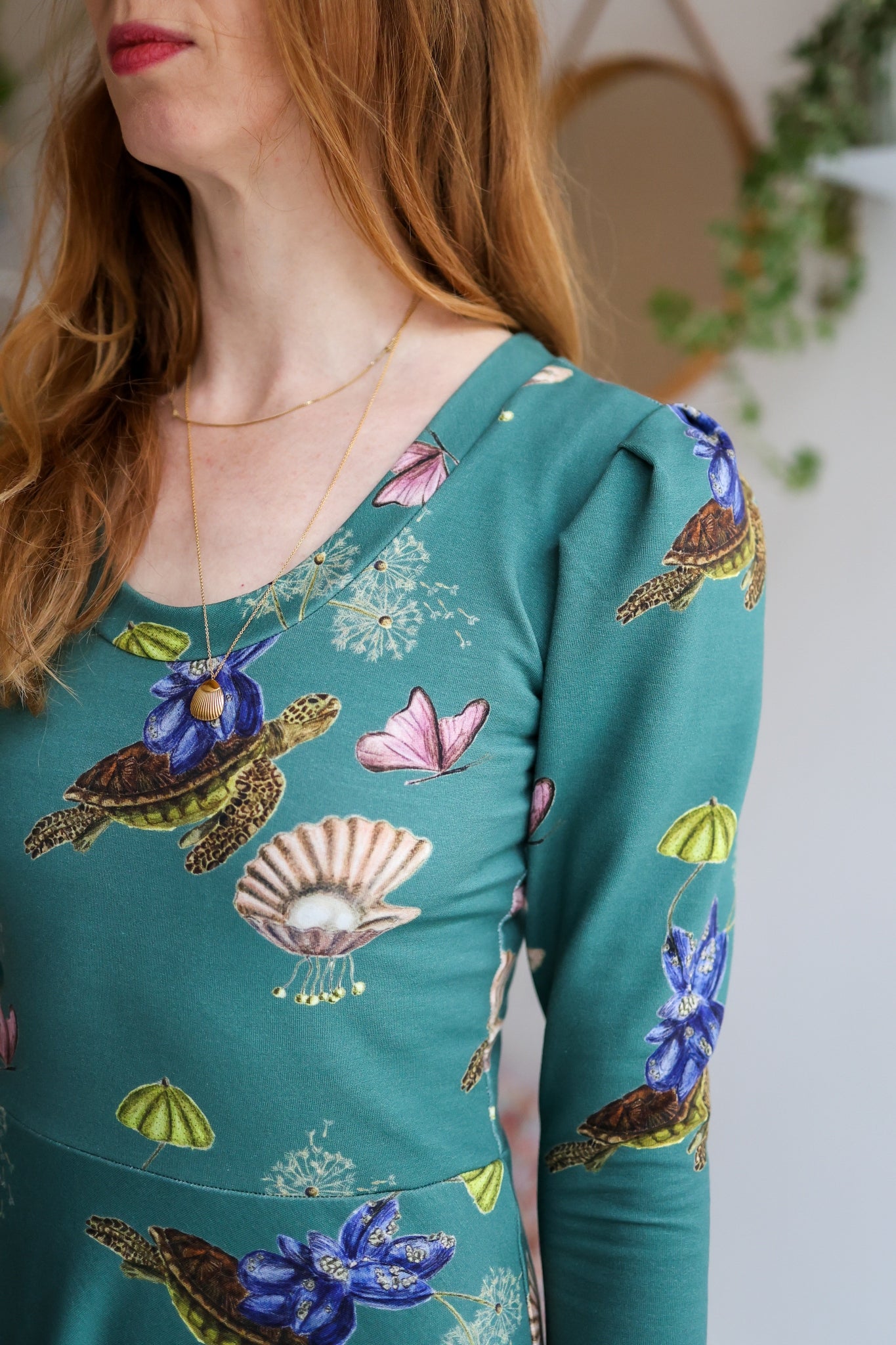 Teal dress with nature-themed print worn by a woman, with a neutral blurred background.