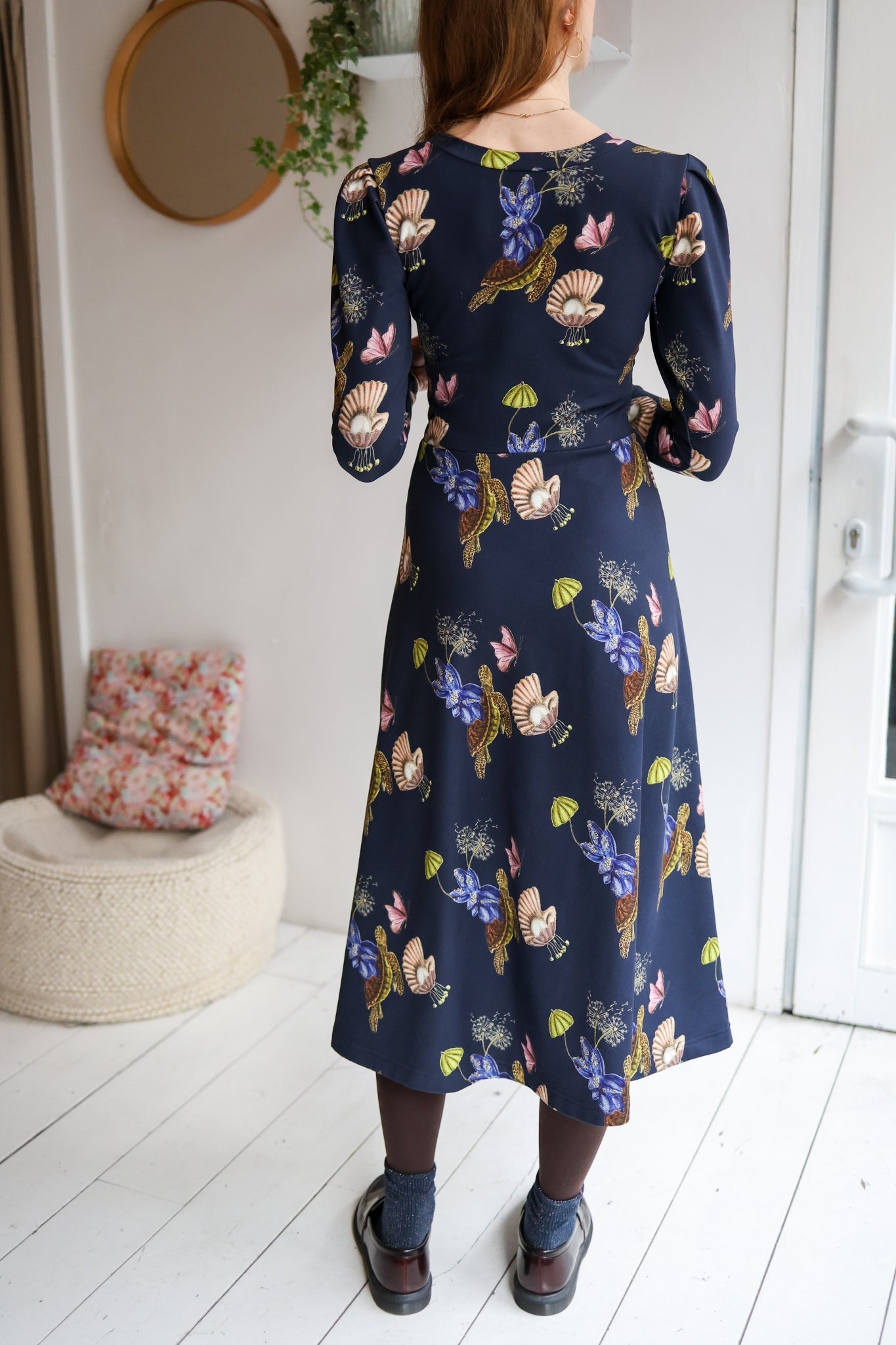 Woman wearing a navy floral dress standing in a room with white walls and wooden floor.