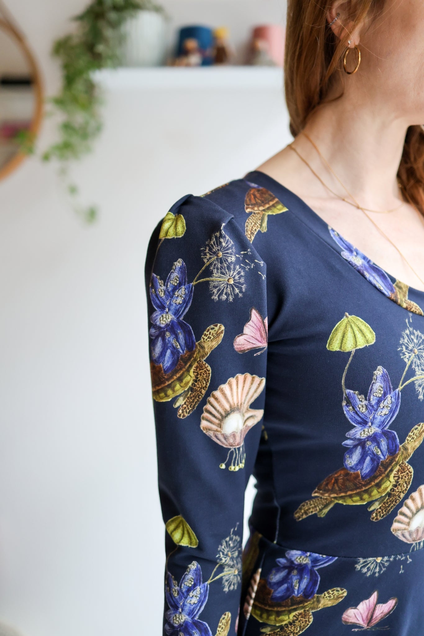Close-up of a woman wearing a navy blue long-sleeve dress with colorful sea-themed pattern with a blurred background.