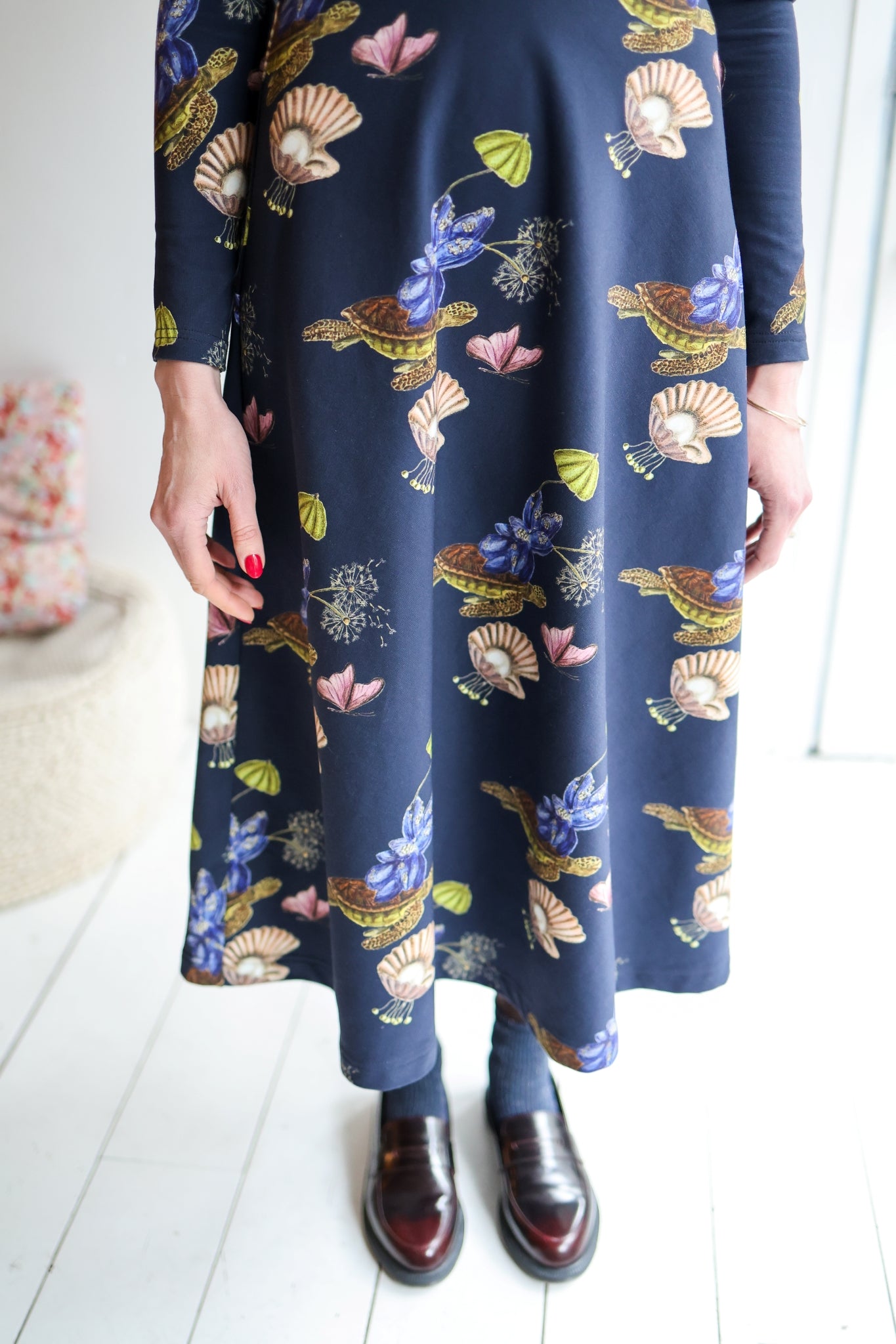 Woman wearing a navy floral dress standing in a room with white walls and wooden floor.