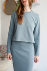 Woman wearing a light blue outfit with a matching skirt in a minimal indoor setting.