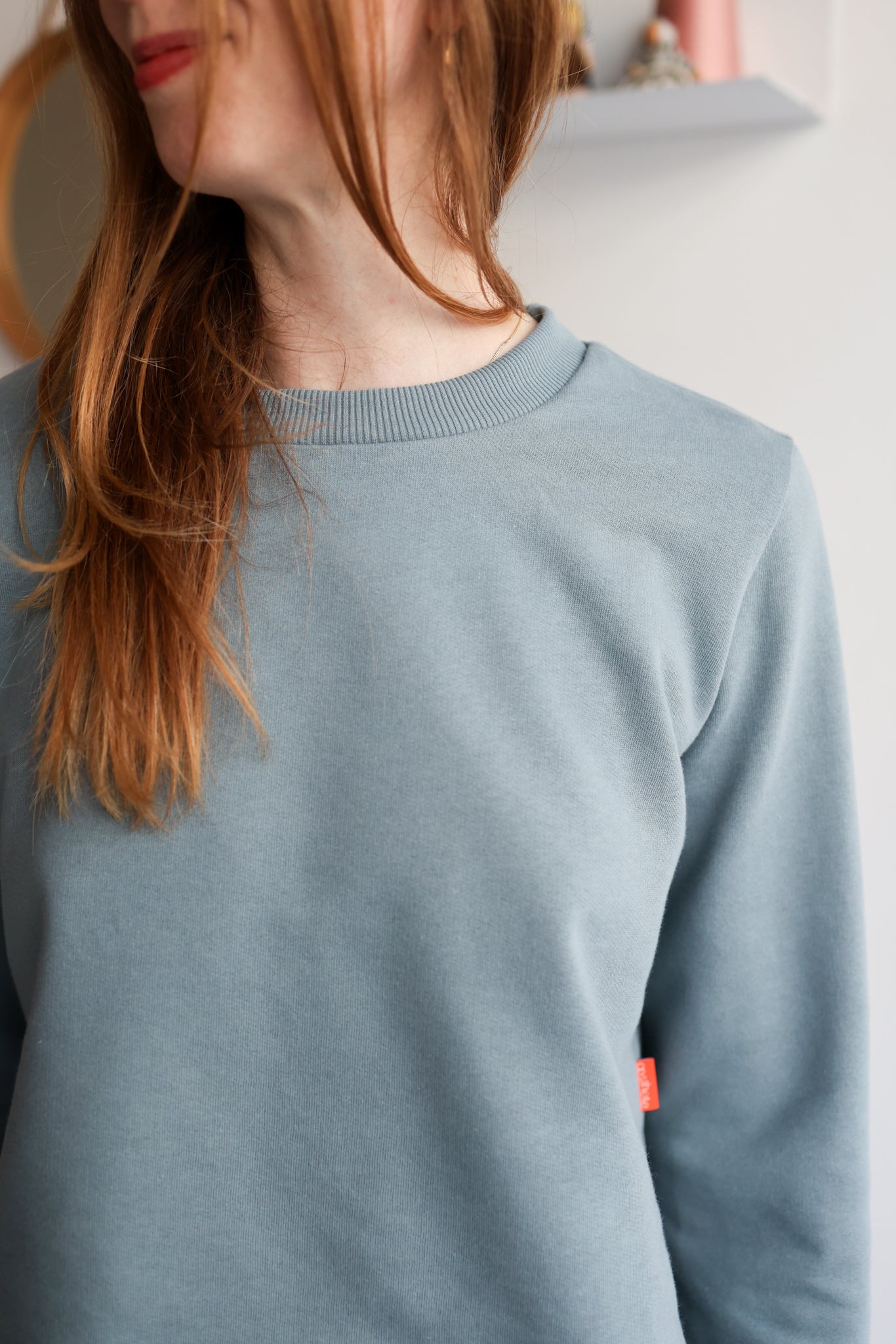 Close-up of a woman wearing a light blue sweater in a room with a blurred background.
