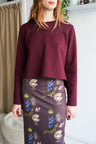 Woman wearing a bordeaux sweatshirt and a patterned skirt indoors.