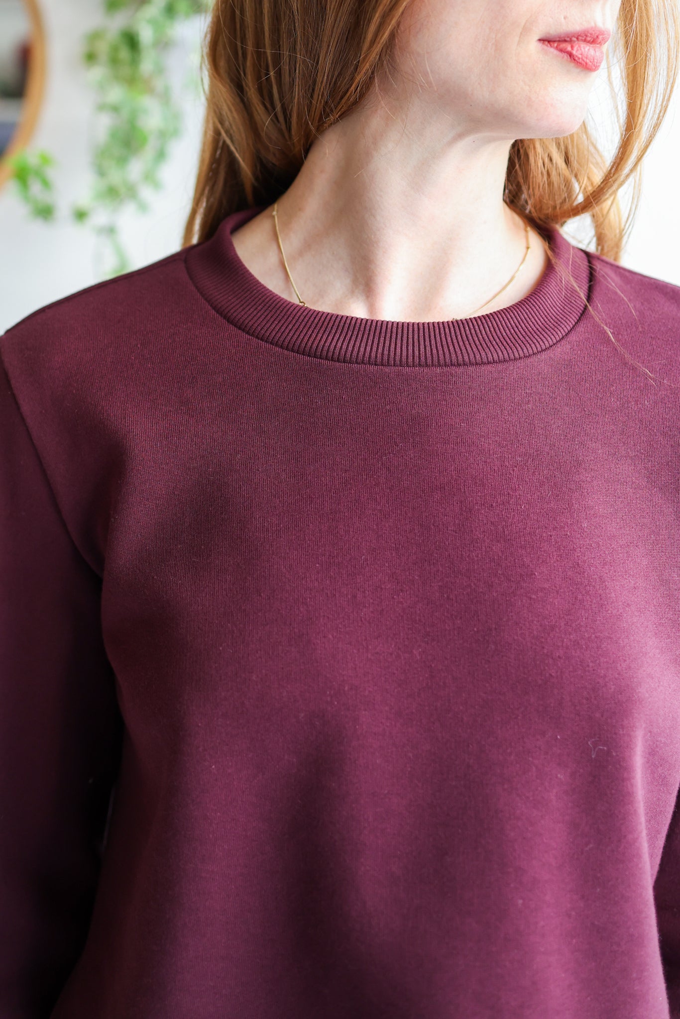 Close-up of a woman wearing a bordeaux sweatshirt with a blurred background.
