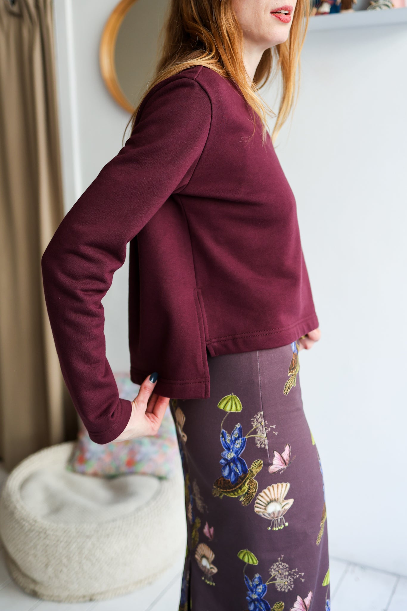 Woman wearing a bordeaux sweatshirt and patterned skirt indoors.