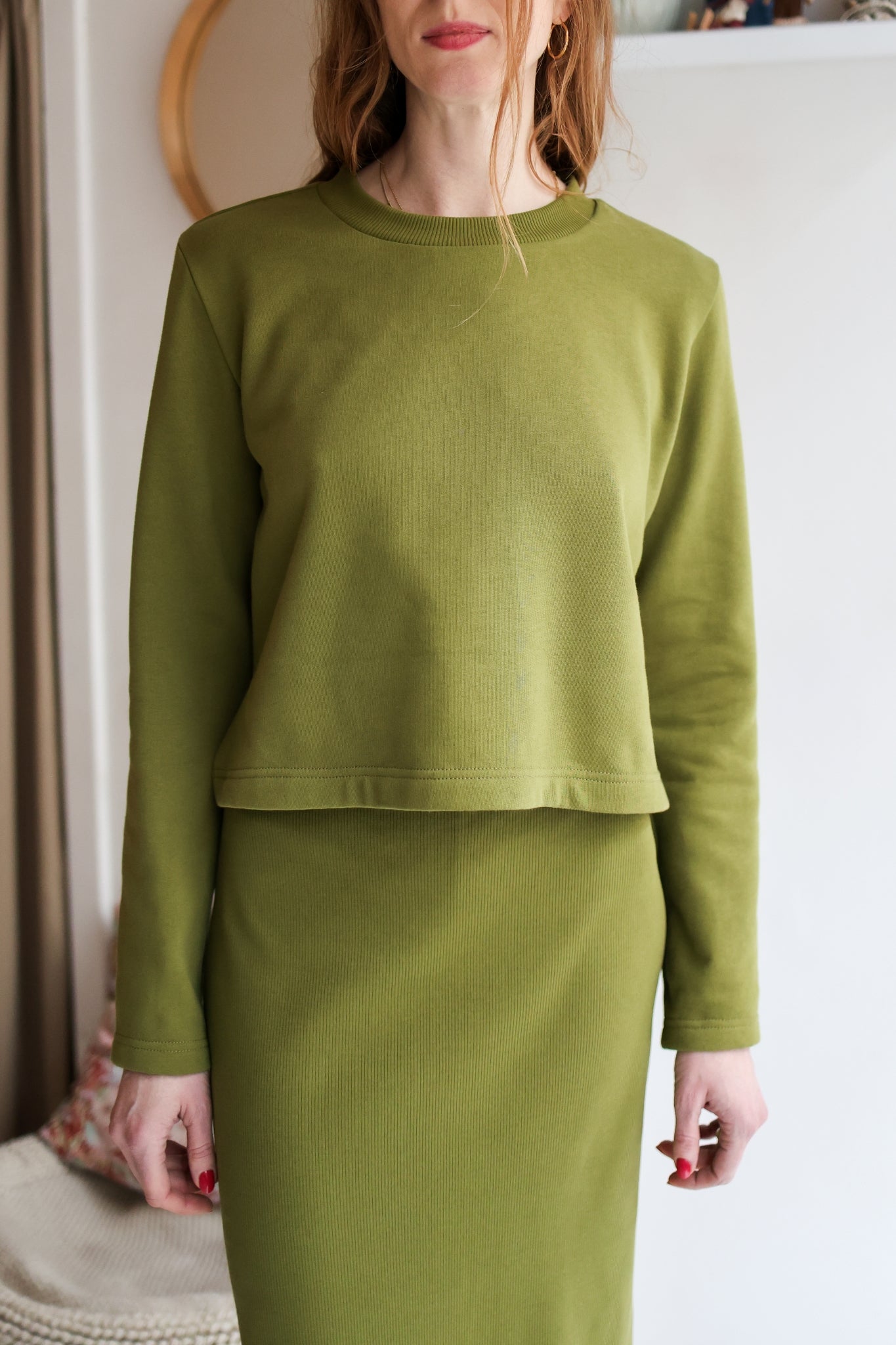 Person wearing a green long-sleeve top and skirt set indoors.