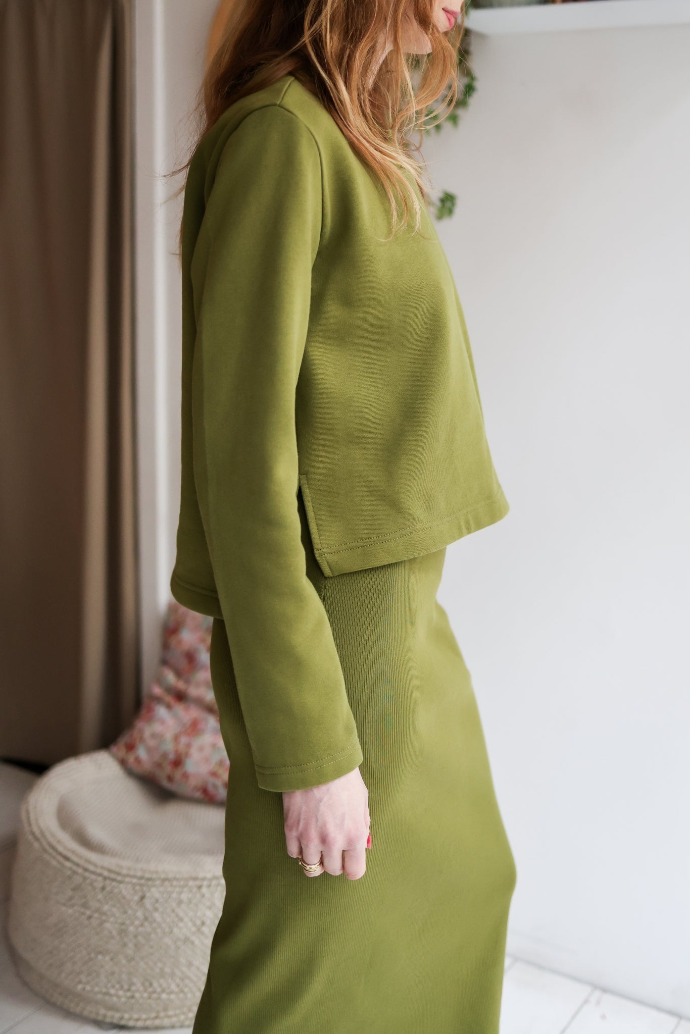 Person wearing a green suit standing indoors with a neutral background.