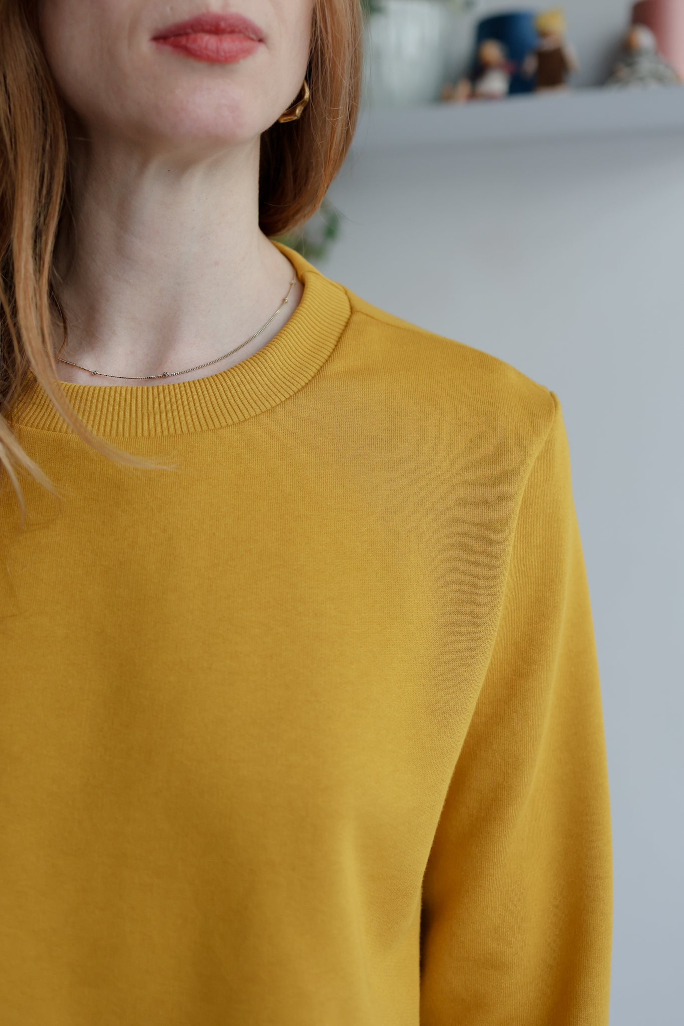 Close-up of a woman wearing a yellow sweatshirt with a blurred background.