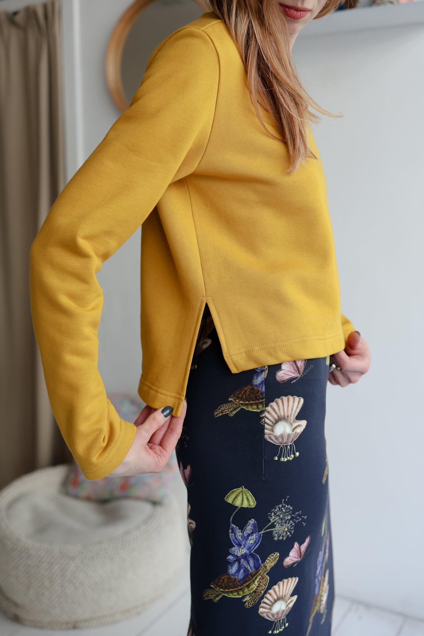Woman wearing a yellow sweatshirt and  a navy patterned skirt with a blurred background.