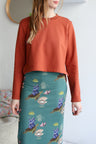 Person wearing a rust-colored top and a teal skirt with floral patterns.