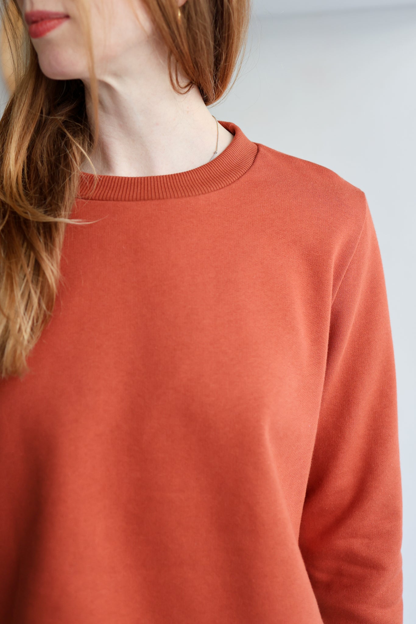Person wearing a rust-colored sweater against a light background