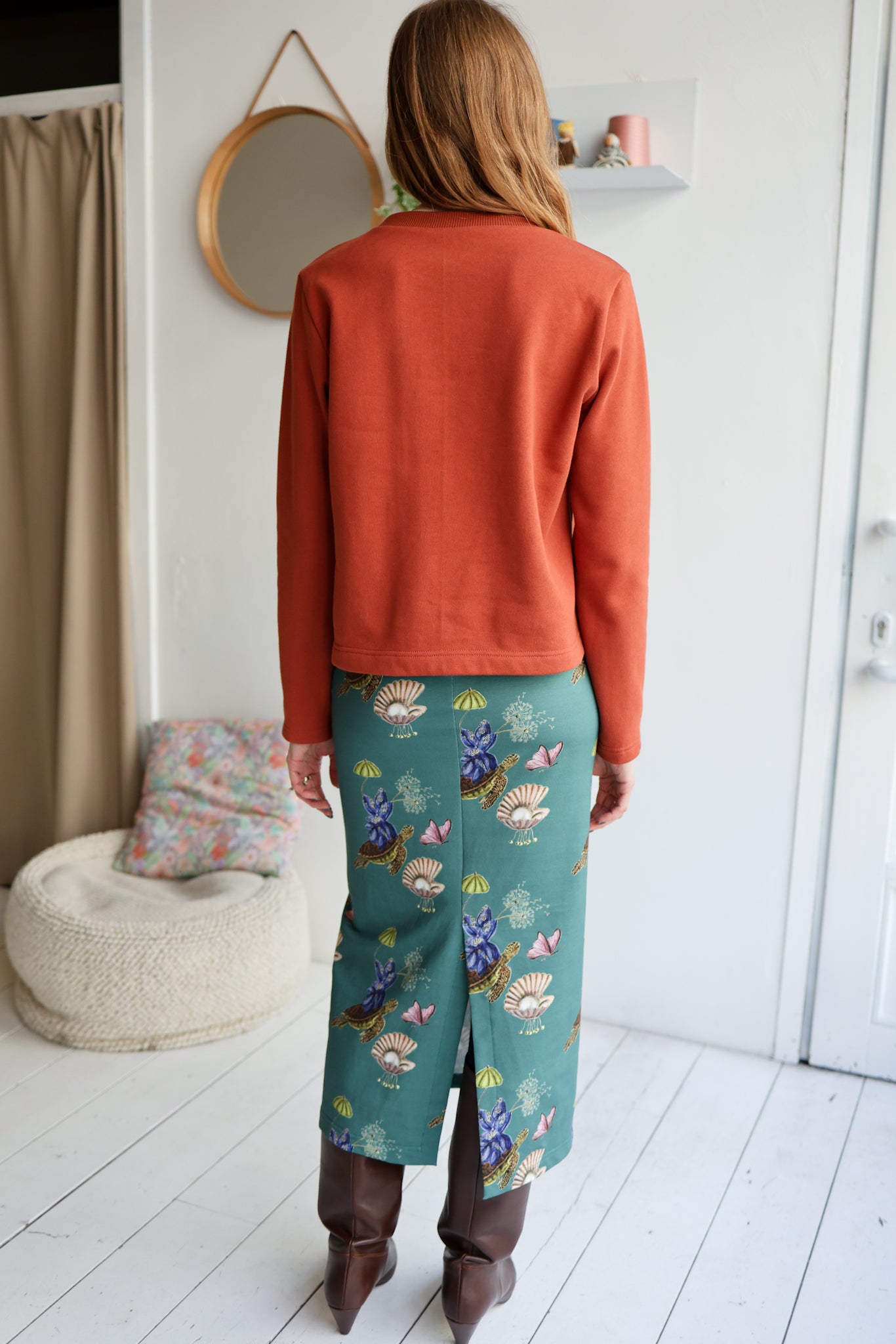 Woman wearing an orange sweater and teal pants with floral pattern in a room.