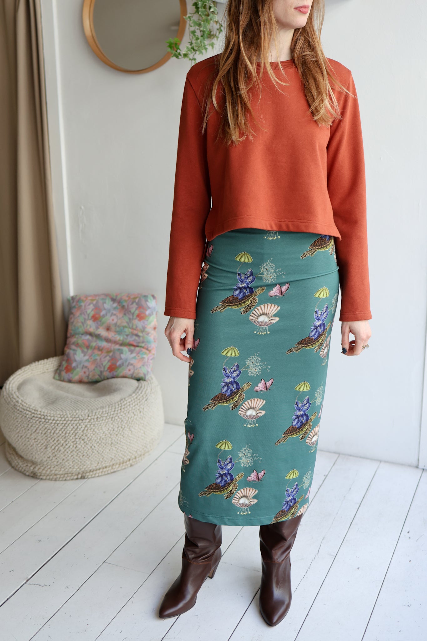 Woman wearing a rust-colored top and teal skirt with floral patterns in a room.