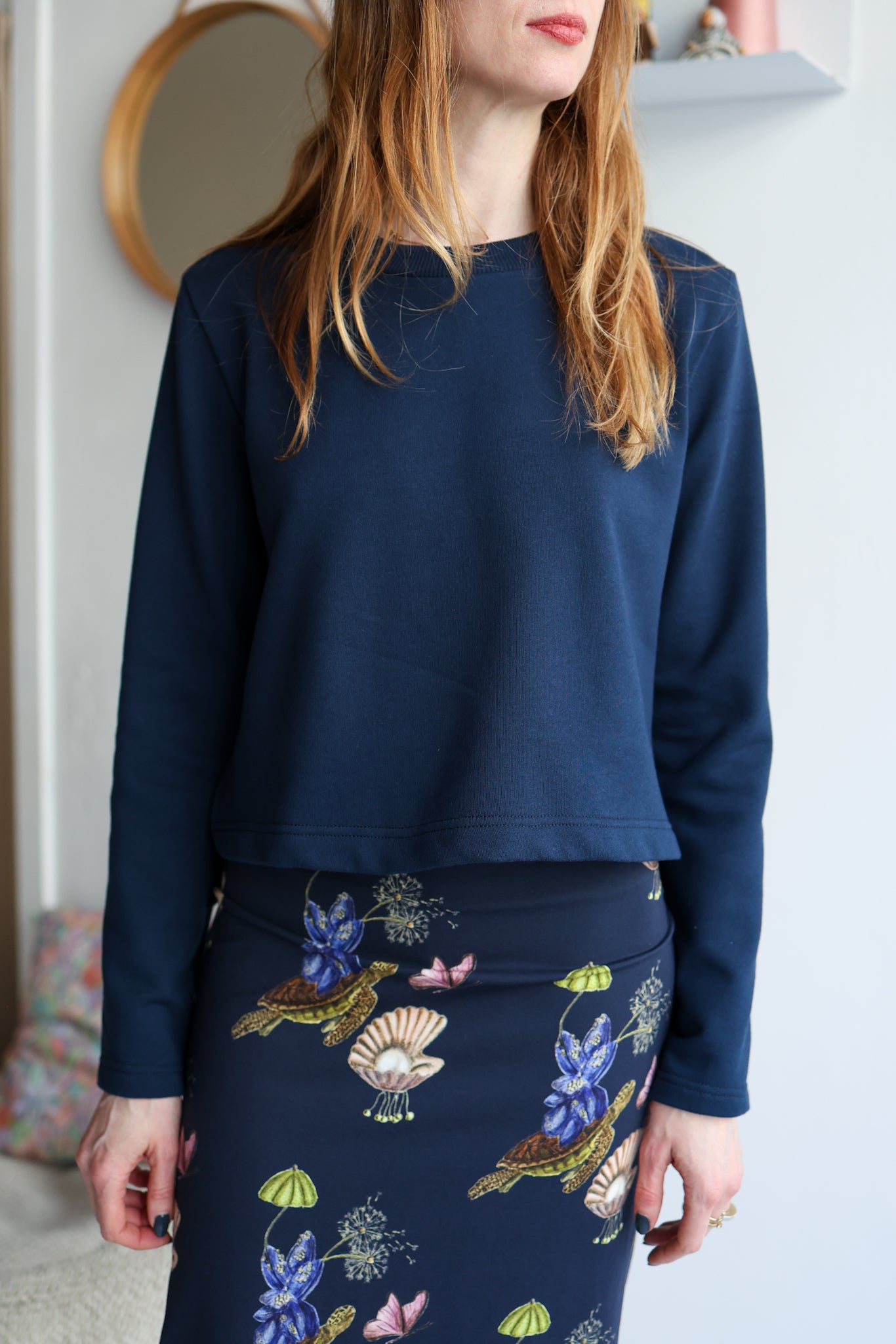 Woman wearing a navy blue top and a navy floral skirt indoors.