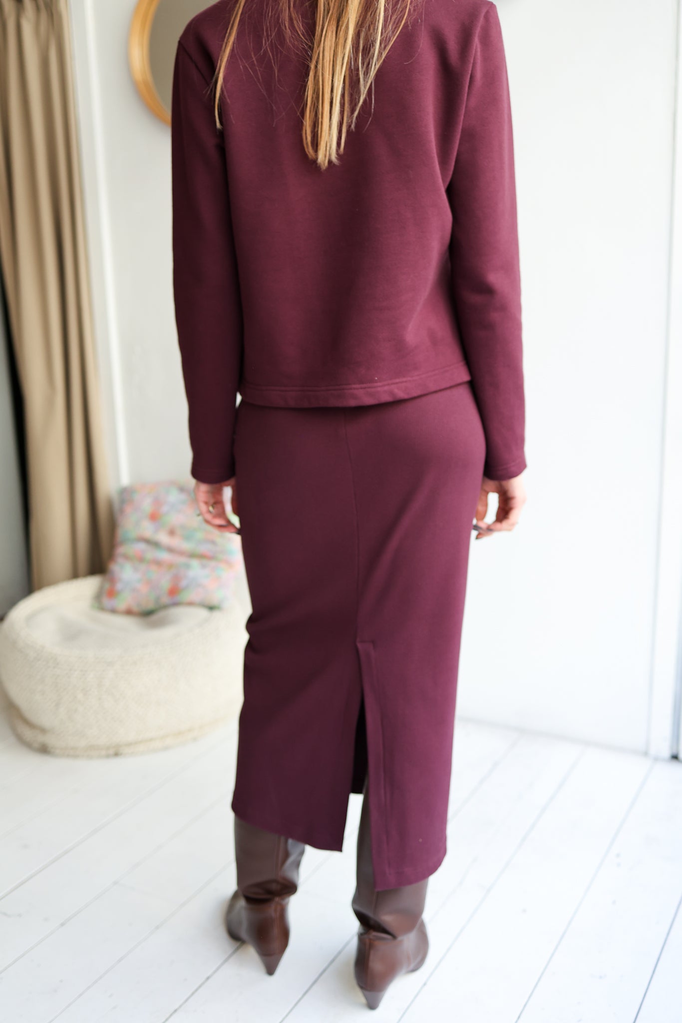 Person wearing a burgundy outfit standing in a room with white walls and a curtain.
