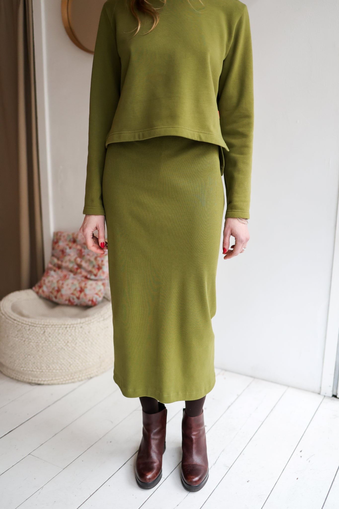 Person wearing a green outfit with a skirt and top, standing indoors.