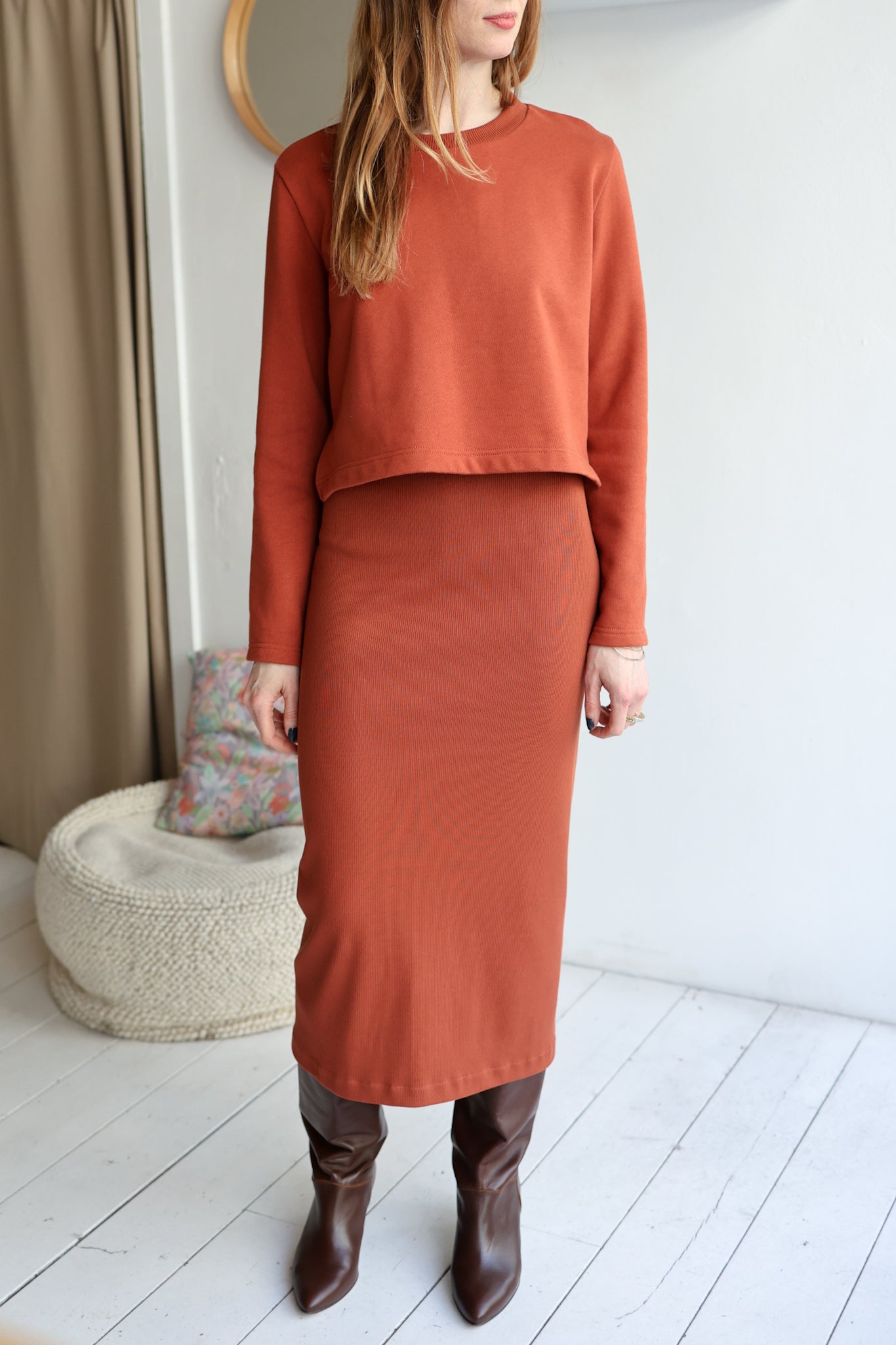 Woman wearing a rust-colored outfit with a skirt and top in a minimalistic room.