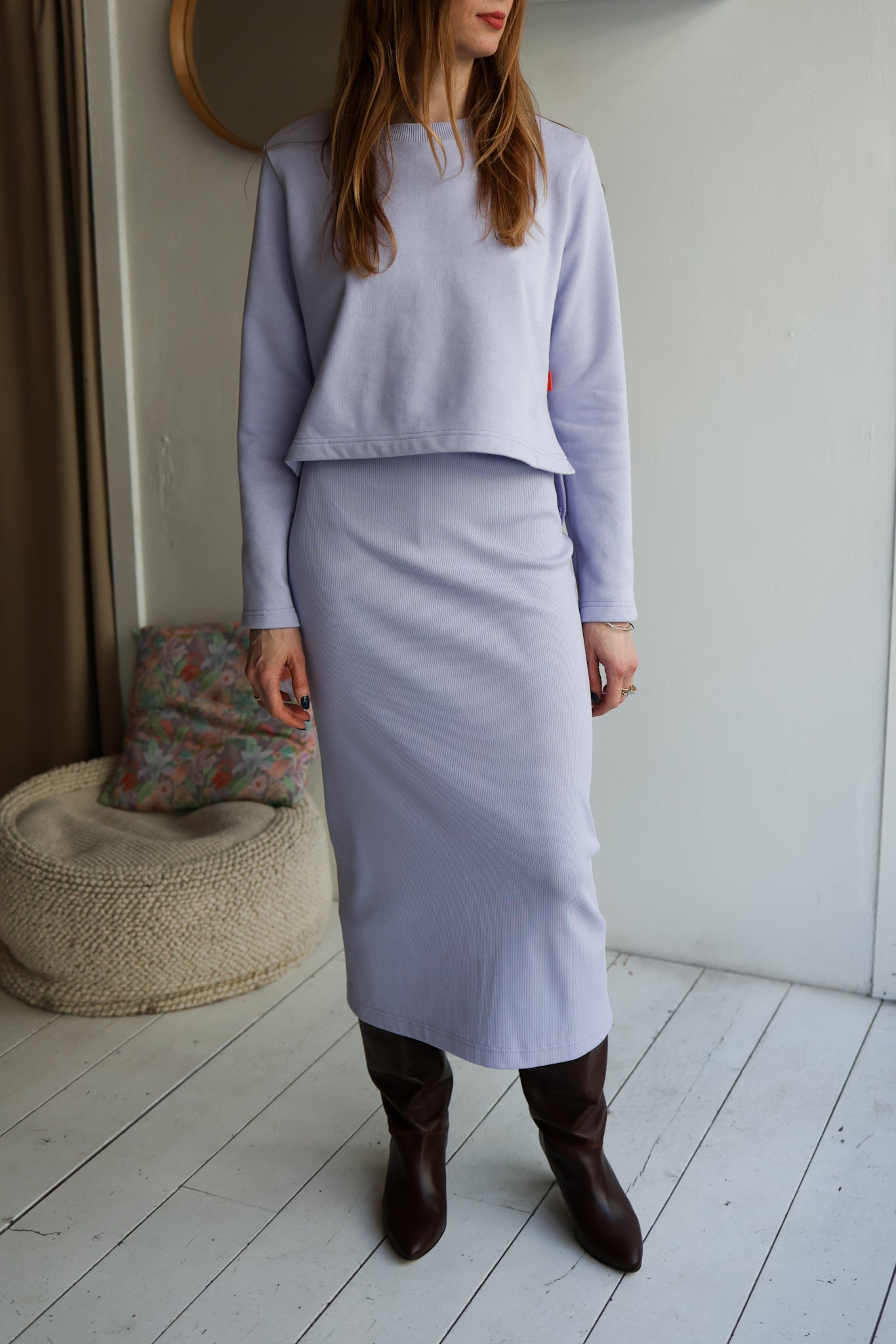 Person wearing a light purple outfit with a skirt and sweater in a minimalistic room.