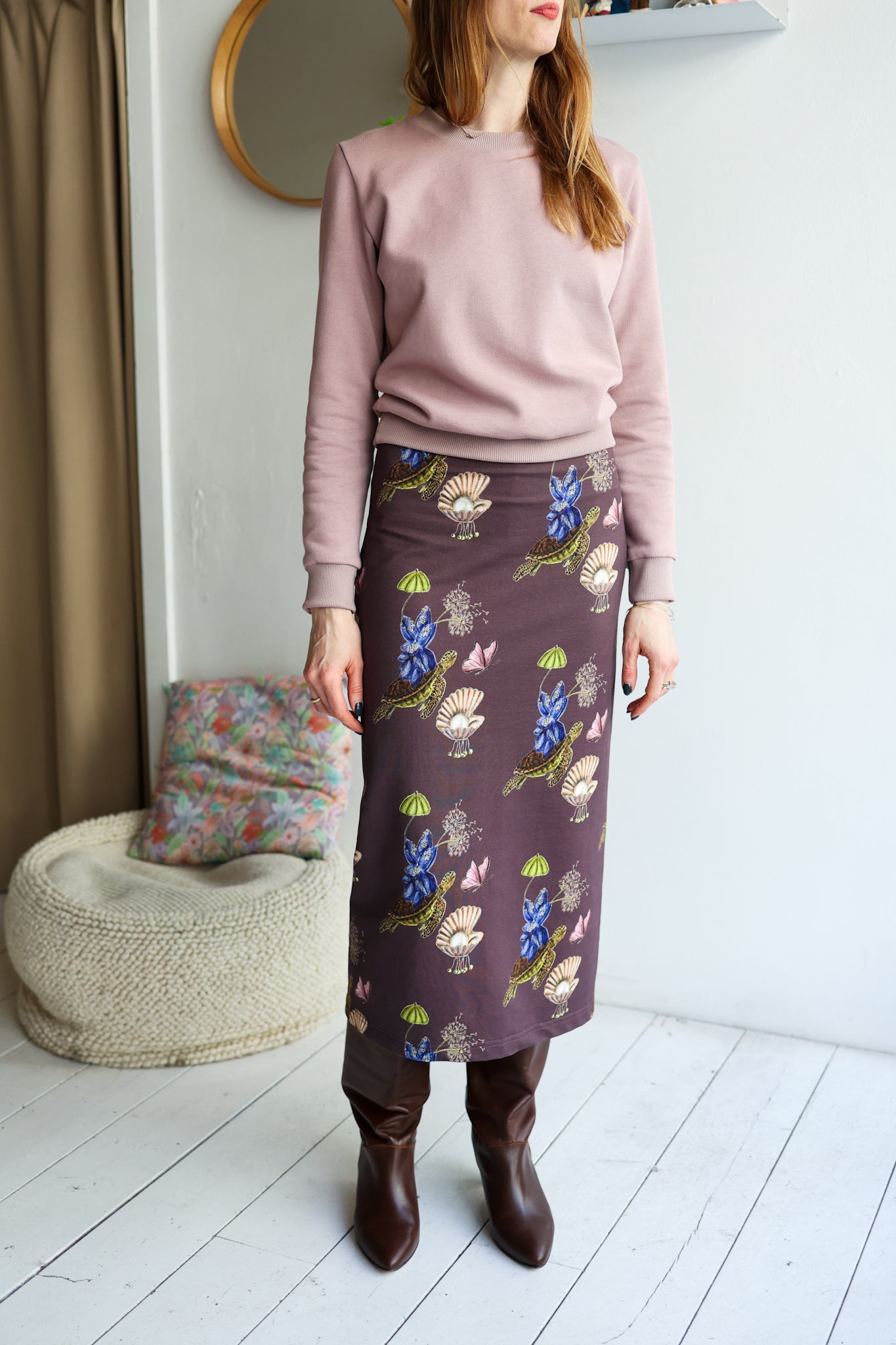 Woman wearing a pink sweater and patterned skirt in a room with a mirror and bean bag chair.