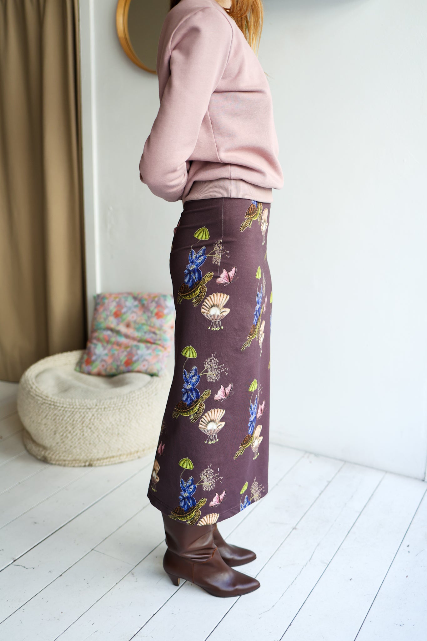 Person wearing a floral-patterned skirt in a room with a white wall and wooden floor.
