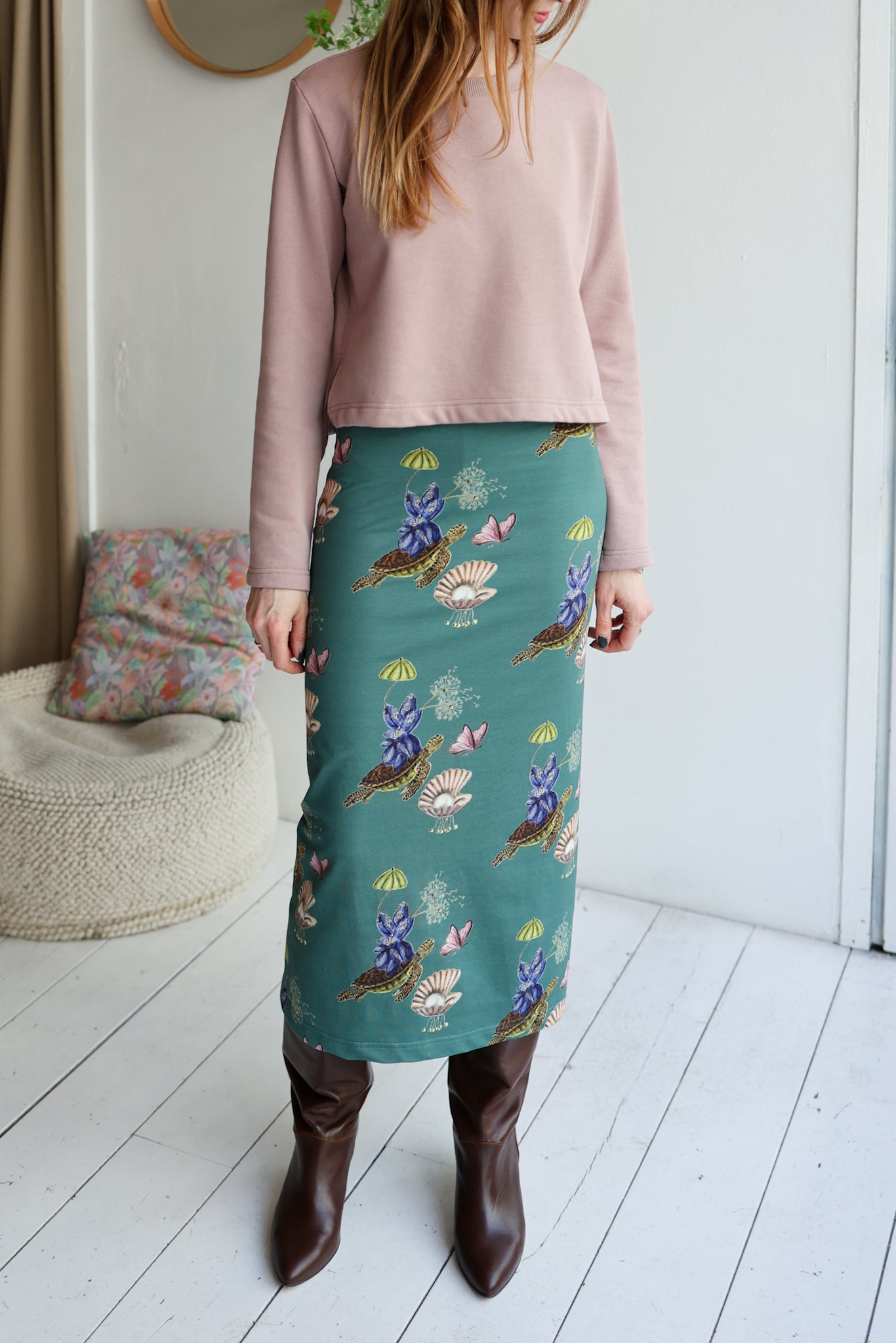Person wearing a pink top and teal skirt with floral patterns indoors.