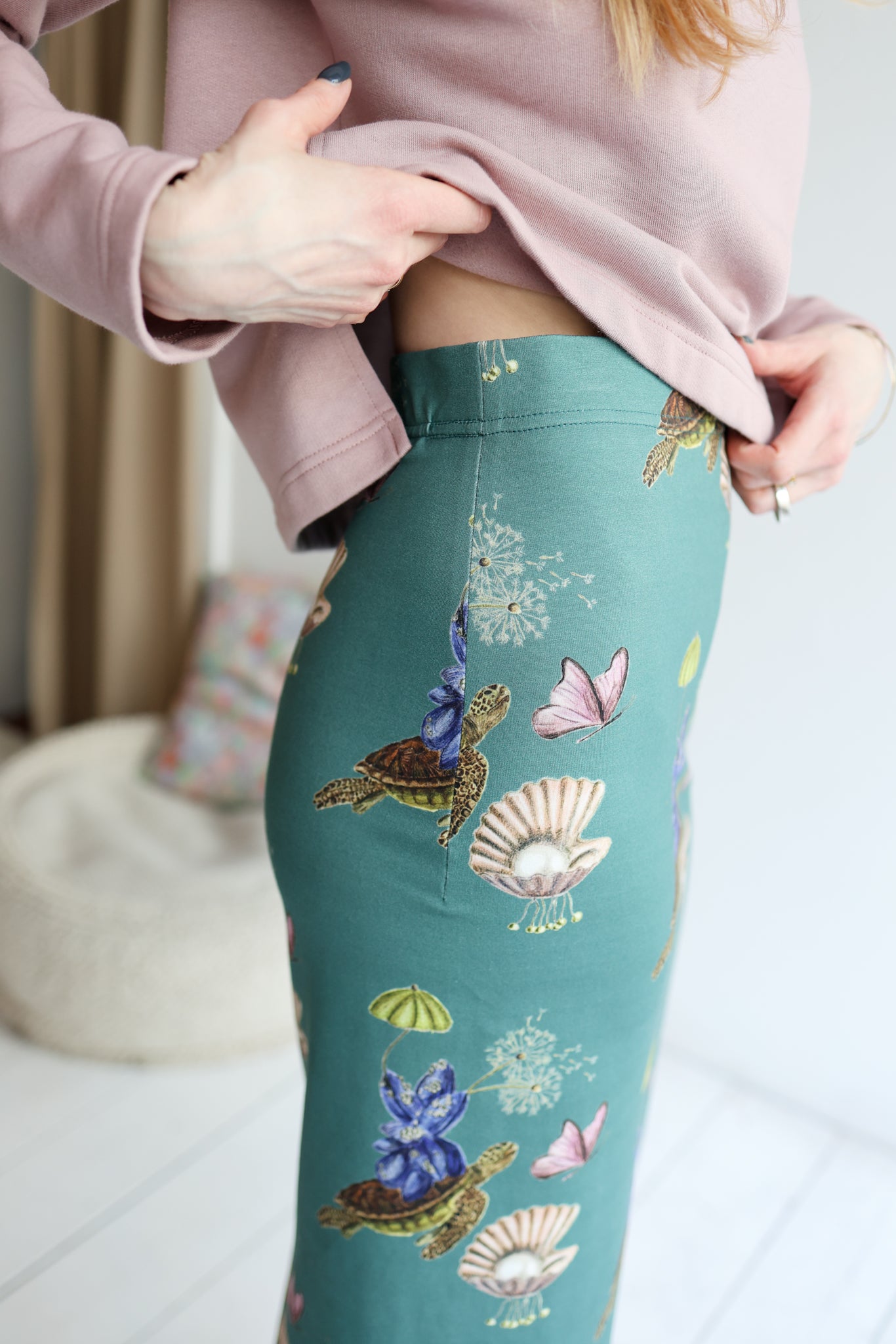 Person wearing teal leggings with turtle and shell design, standing indoors.