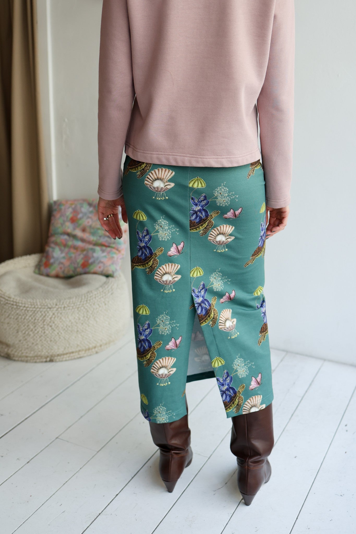Person wearing a pink top and teal skirt with shell pattern on a white floor.