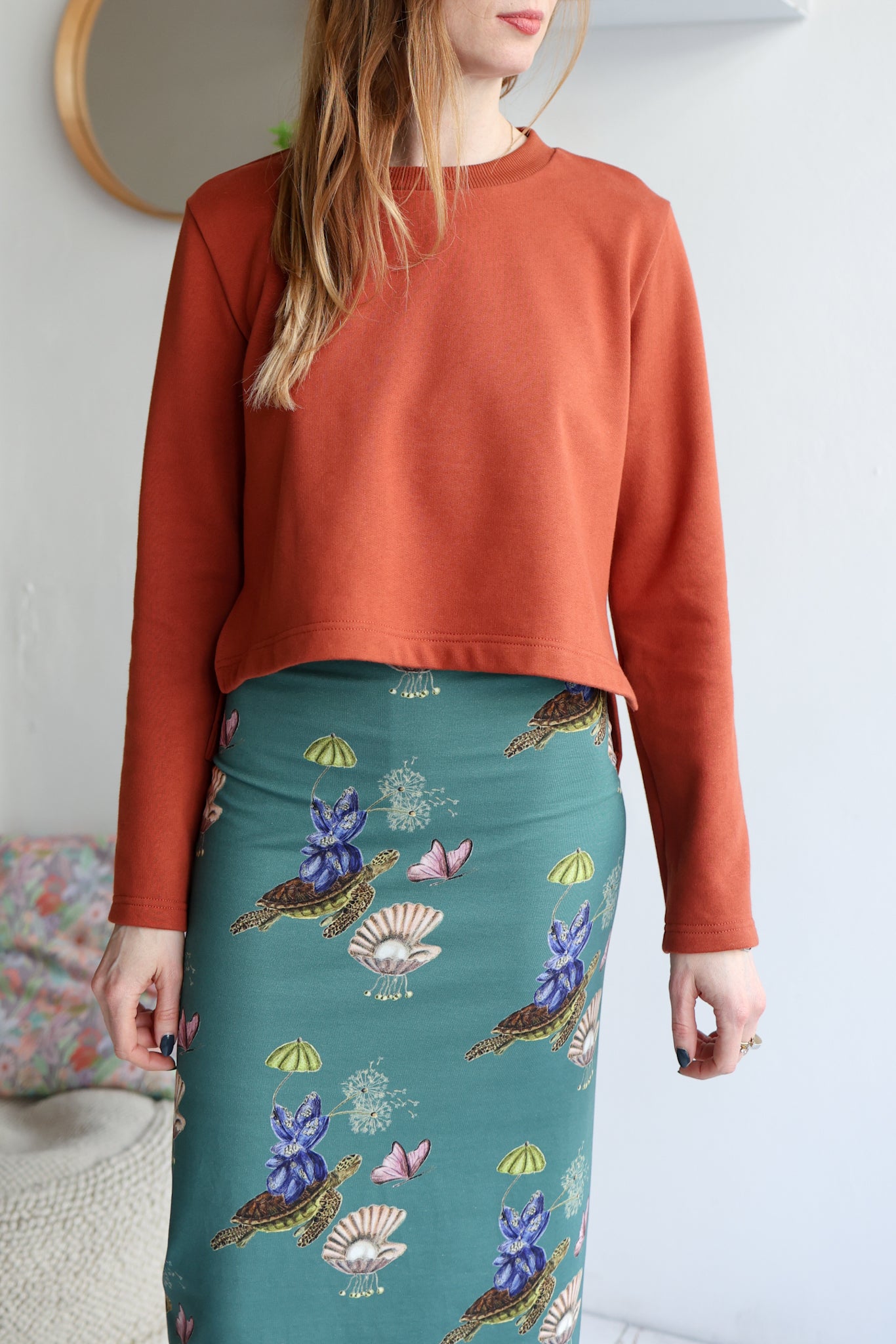 Person wearing a rust-colored top and a teal skirt with floral patterns.