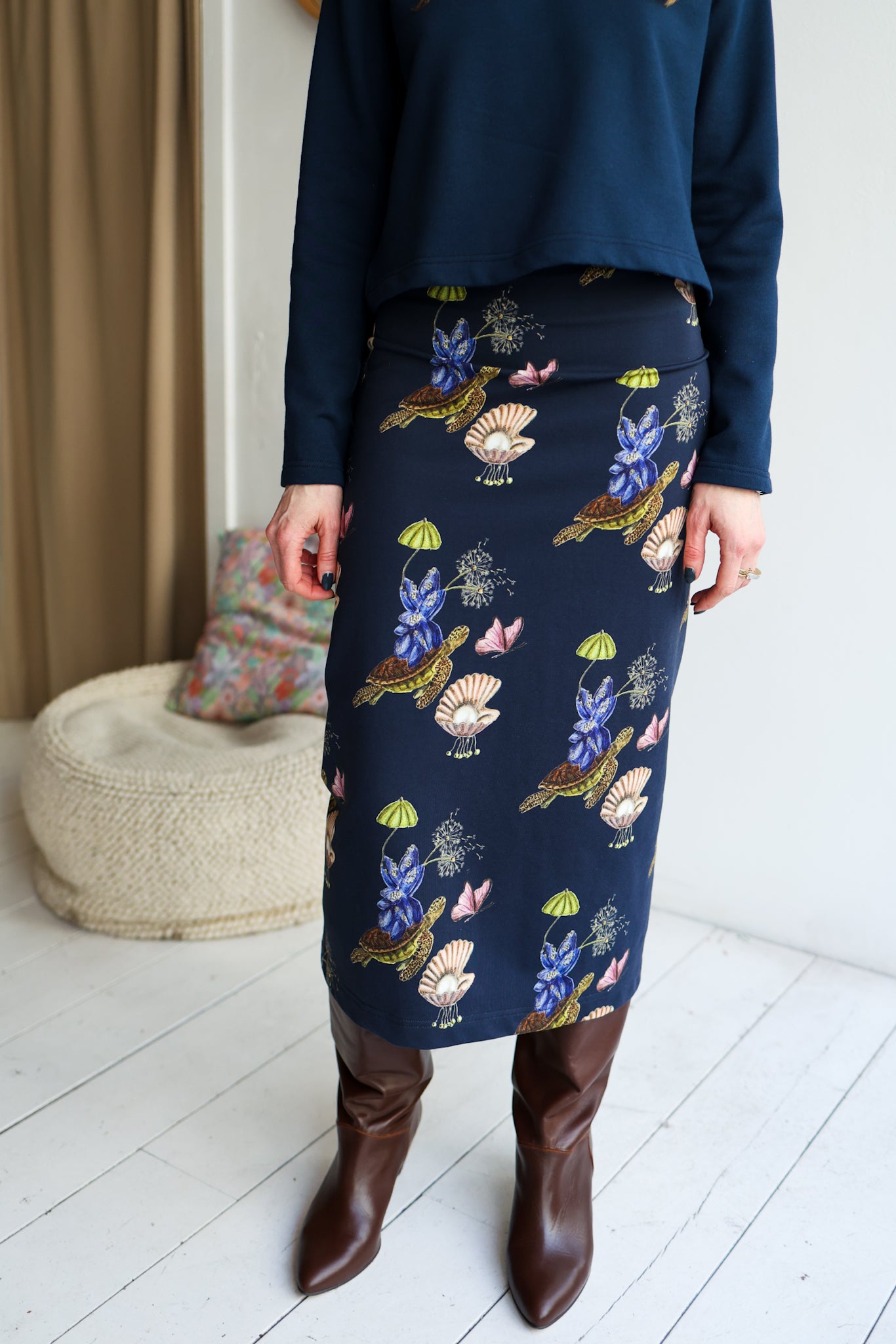 Person wearing a navy skirt with floral patterns and brown knee-high boots indoors.