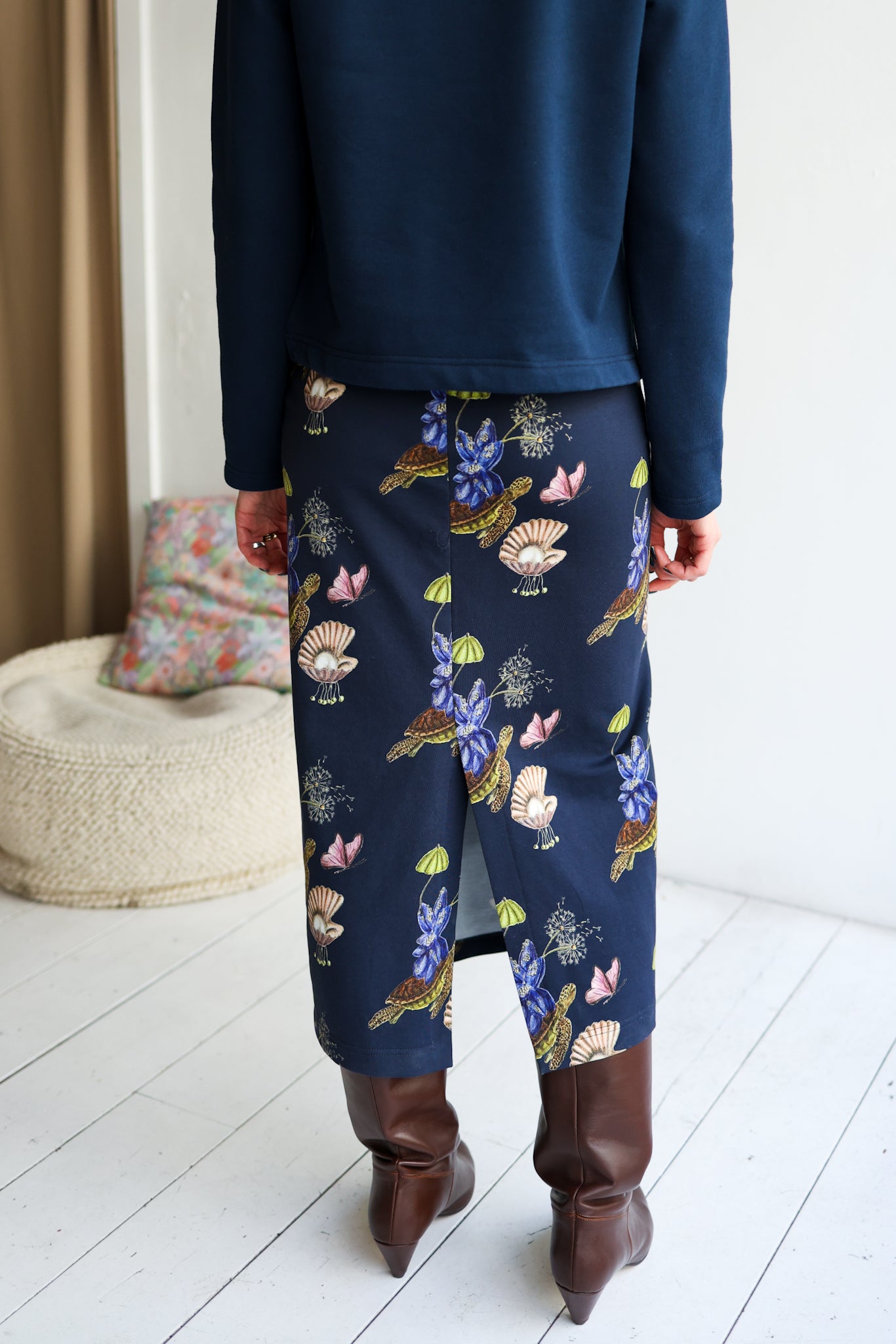 Person wearing a navy blue top and floral-patterned pants in a room with a white floor and a textured chair.