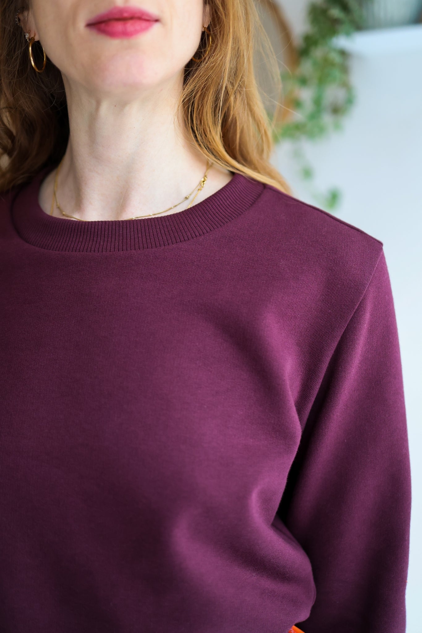 Person wearing a bordeaux sweatshirt in a room with a white wall.
