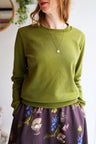 Person wearing a green sweater and floral skirt indoors.