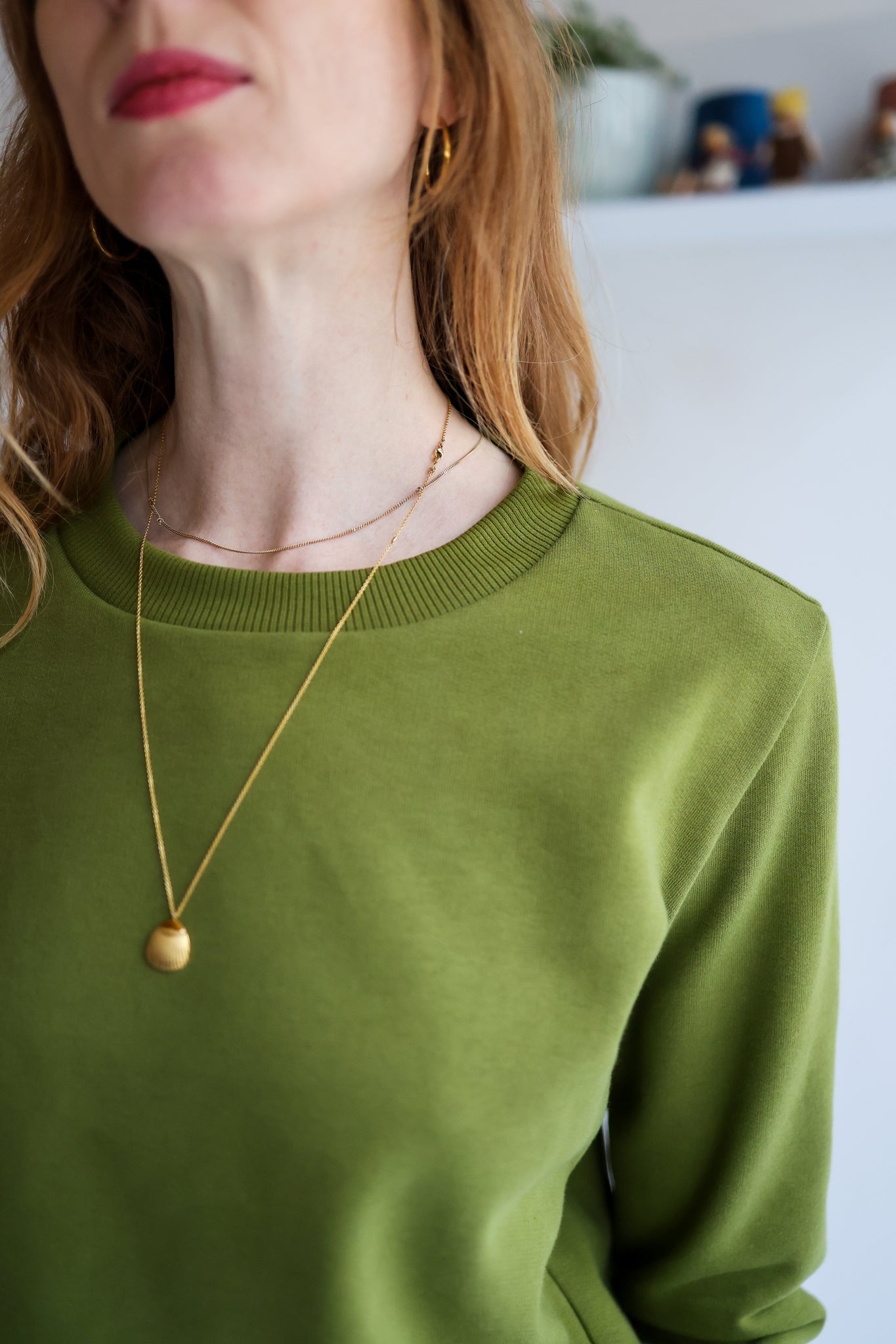 Person wearing a green sweater with a gold necklace