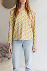Woman wearing a floral patterned loose long sleeve t-shirt and jeans indoors.